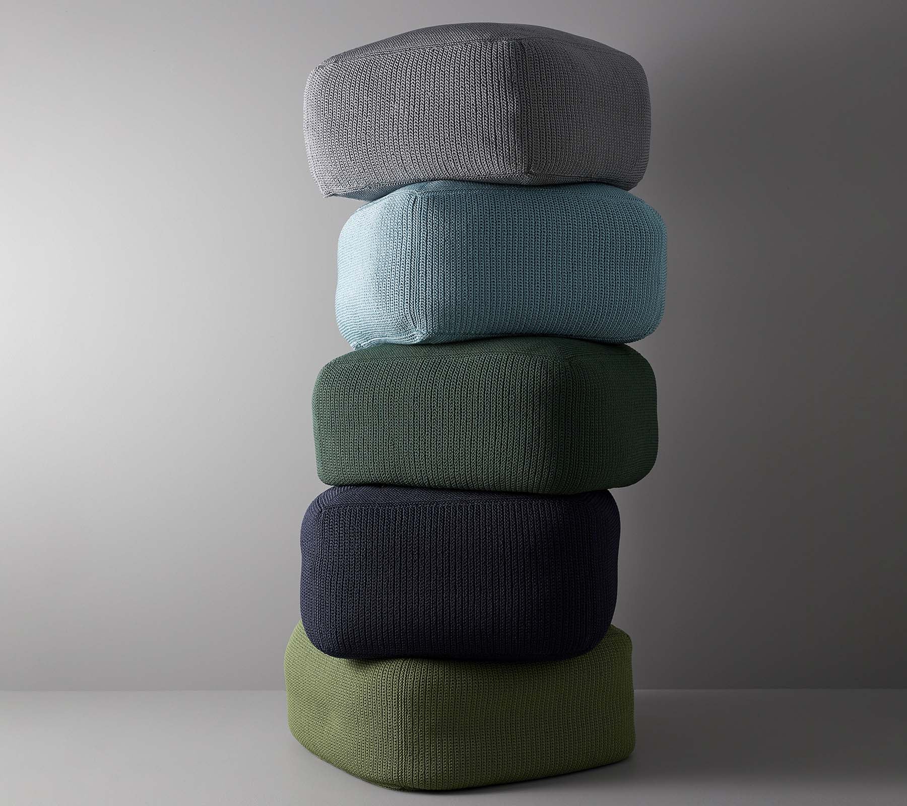 Un arrangement empilé de cinq coussins de différentes couleurs, y compris gris, bleu ciel, vert, bleu foncé et vert olive.