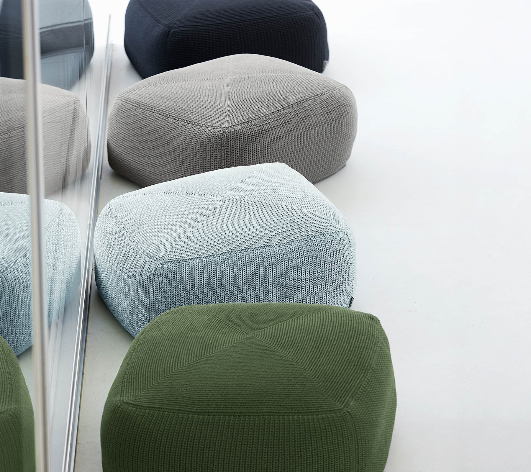 Une collection de poufs colorés et texturés dans diverses teintes, arrangés ensemble, reflétant un design élégant et moderne.