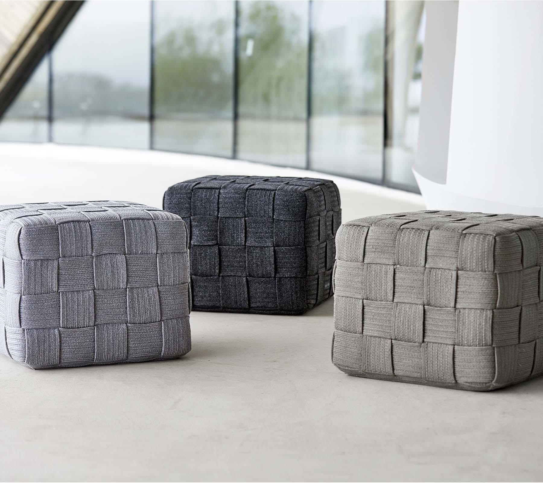 Trois poufs tissés de différentes nuances de gris, avec un design texturé, disposés sur une surface claire. Idéal pour s'asseoir ou pour la décoration.