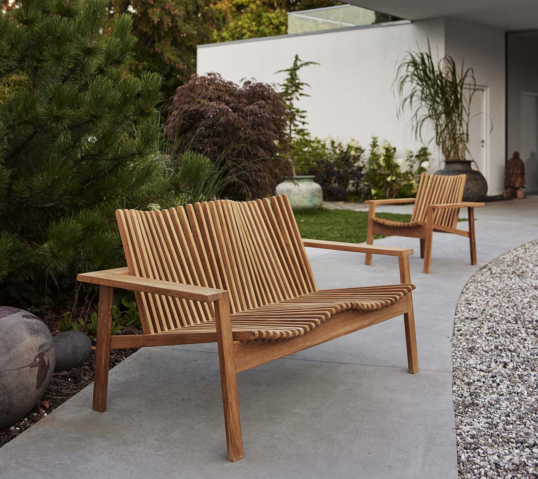 Deux chaises longues en bois Amaze et un canapé assorti présentent un design à lattes, entourés de verdure et d'éléments décoratifs.