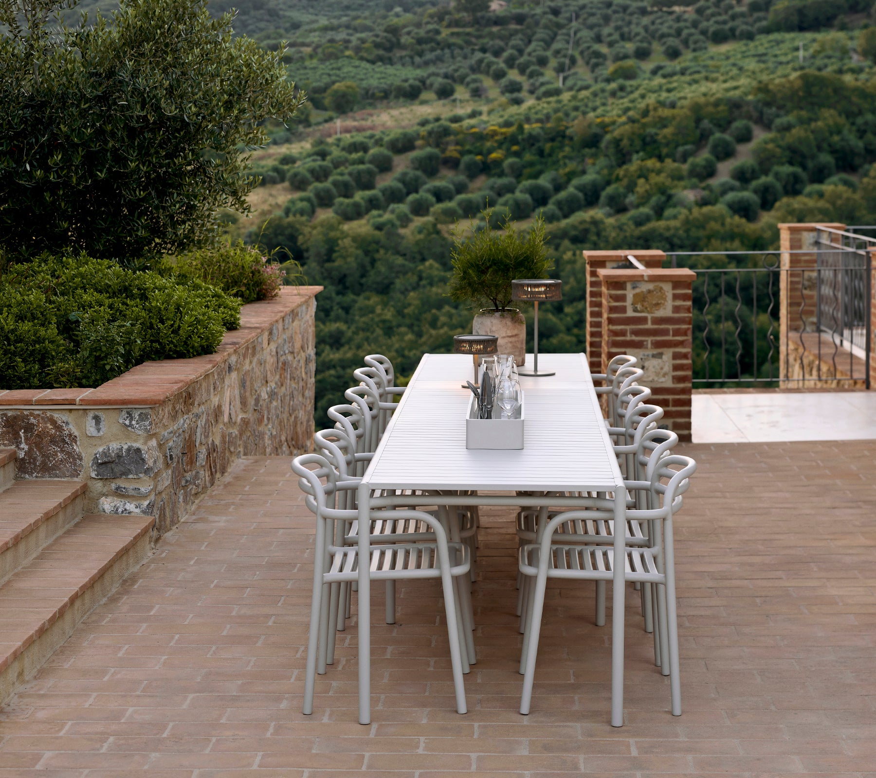 Un aménagement de sièges élégant avec des chaises et une table Bliss en couleur sable, complété par une lampe Illusion, dans un paysage luxuriant.