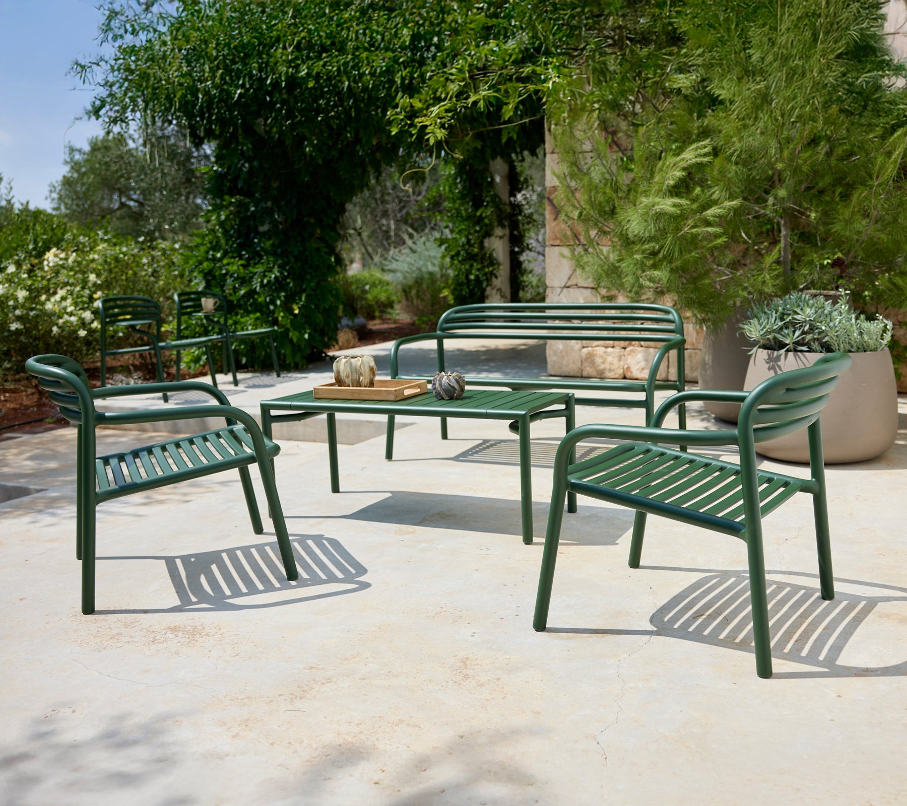 Agencement de sièges extérieurs verts avec des chaises et un banc entourant une table.