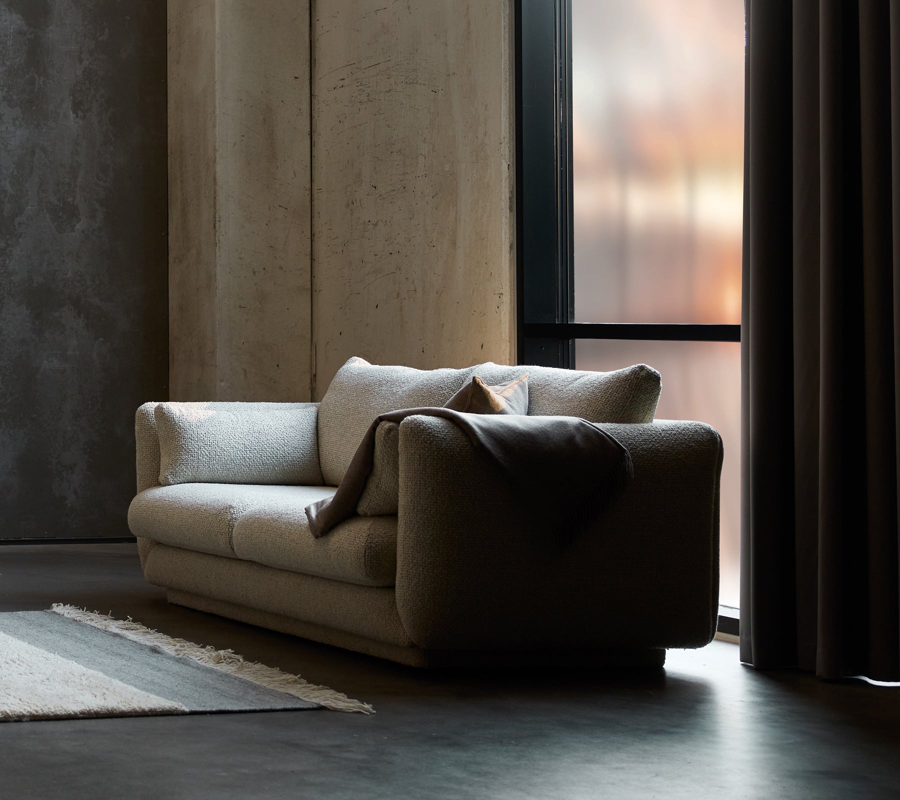 Sofa 2 places Bloom en sable flair, avec un design sur socle et un plaid confortable drapé sur un côté.