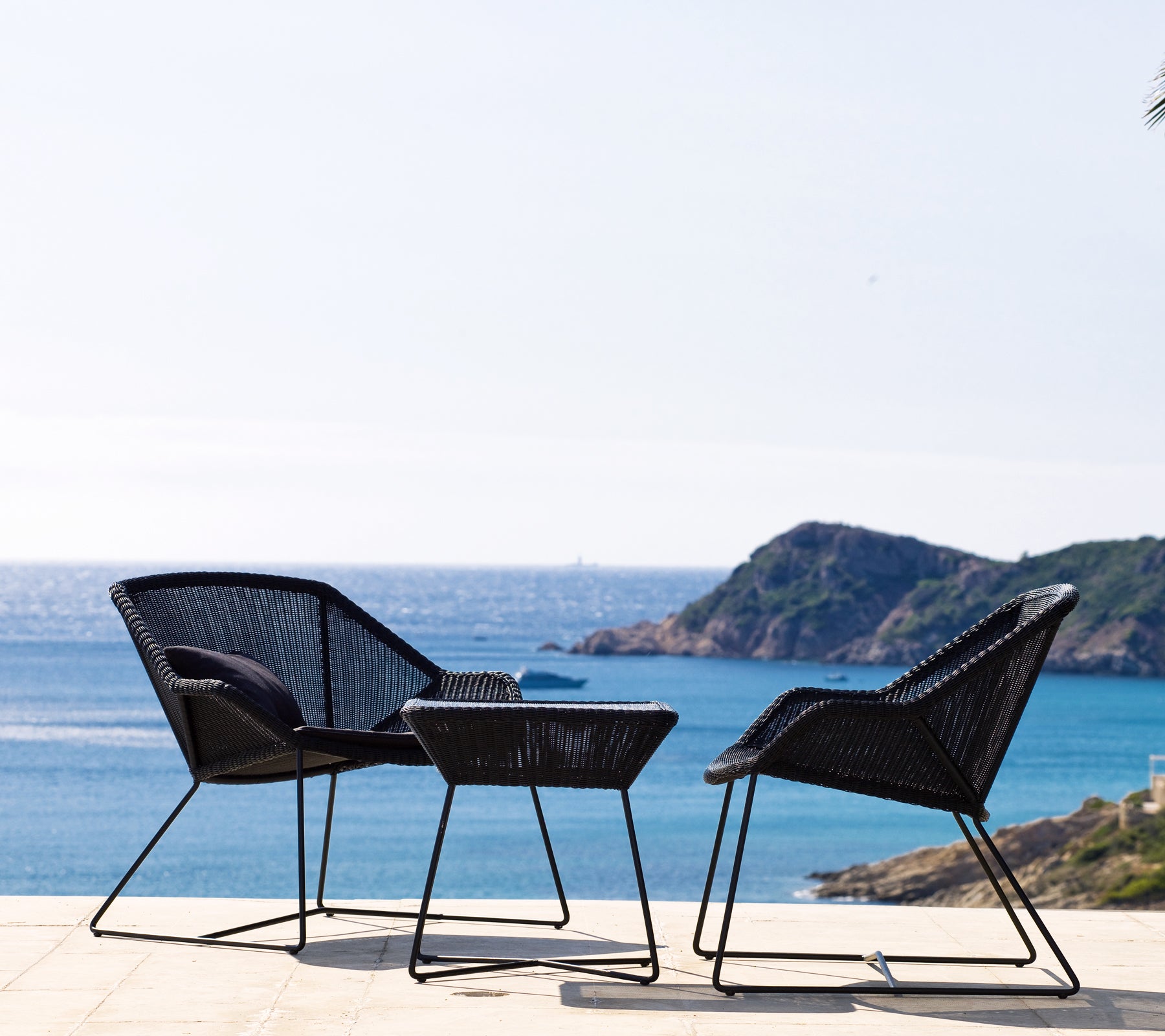 Deux chaises noires et une table noire avec vue sur la côte.