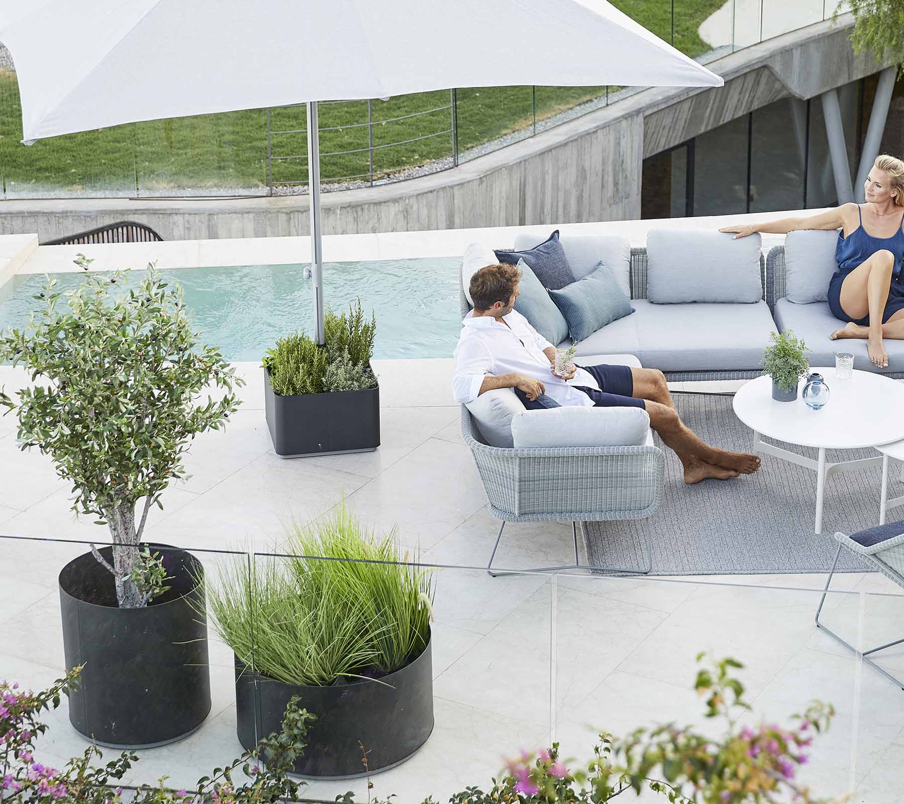 Un espace extérieur élégant avec un canapé confortable, des plantes et un grand parasol, parfait pour se détendre.