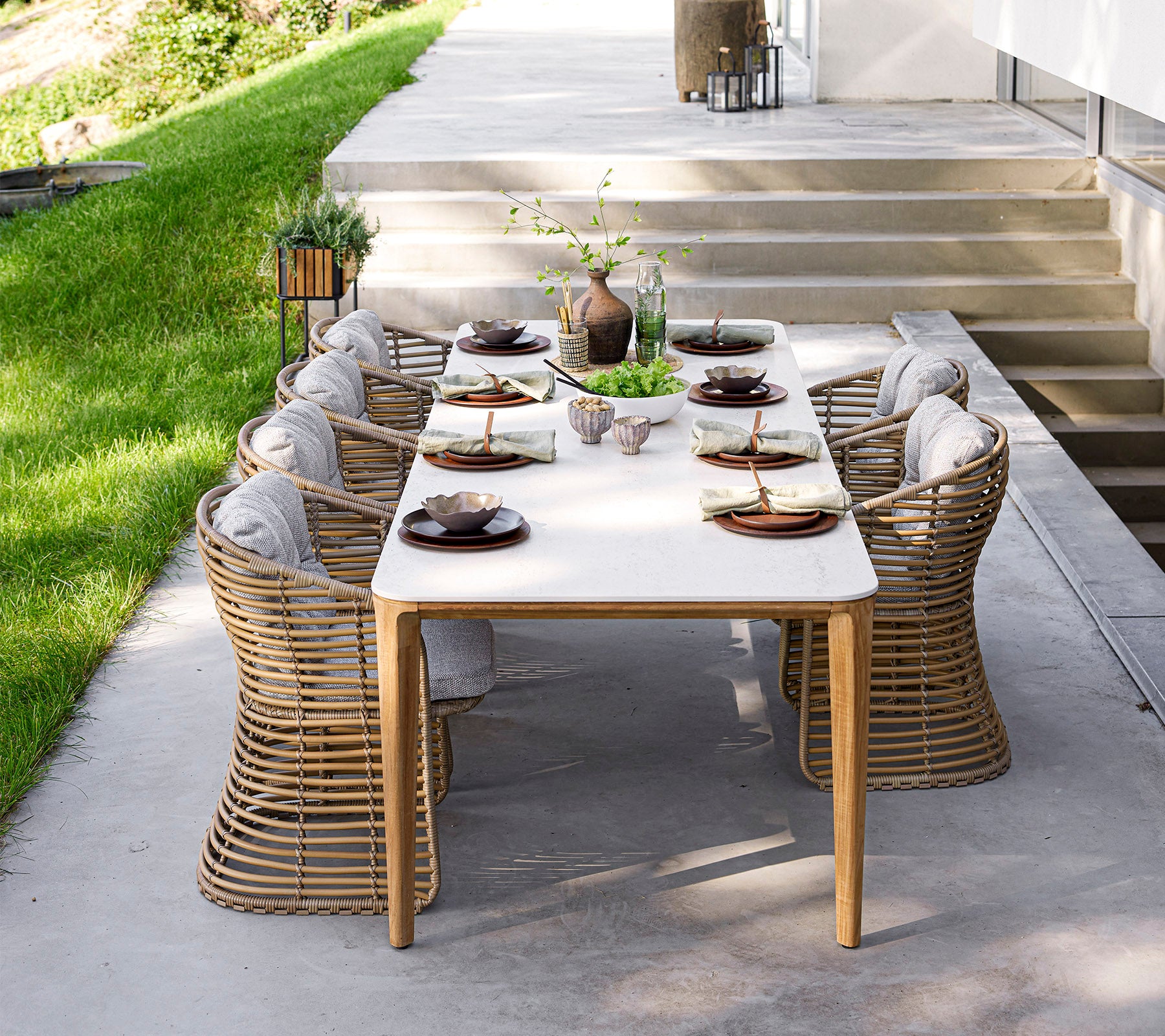 Une table à manger élégante avec de la vaisselle raffinée et des chaises confortables, entourée de verdure et de lumière naturelle. Parfait pour les réunions.