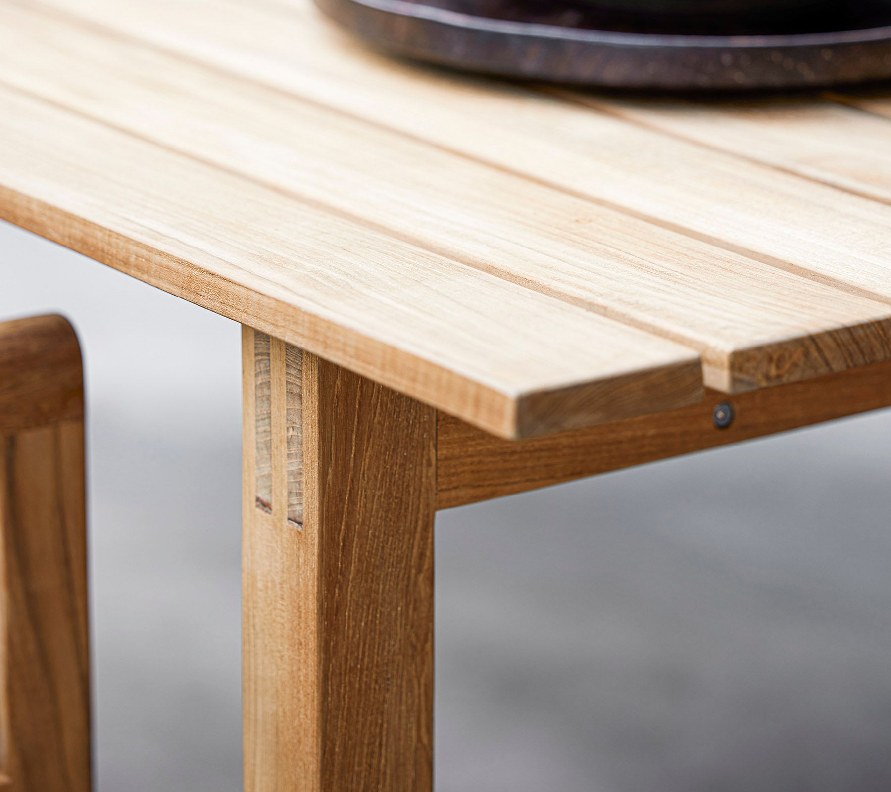 Gros plan d'une table en bois présentant un design à lames et un grand bol décoratif rond sombre sur le dessus. Parfait pour une esthétique de salle à manger moderne.