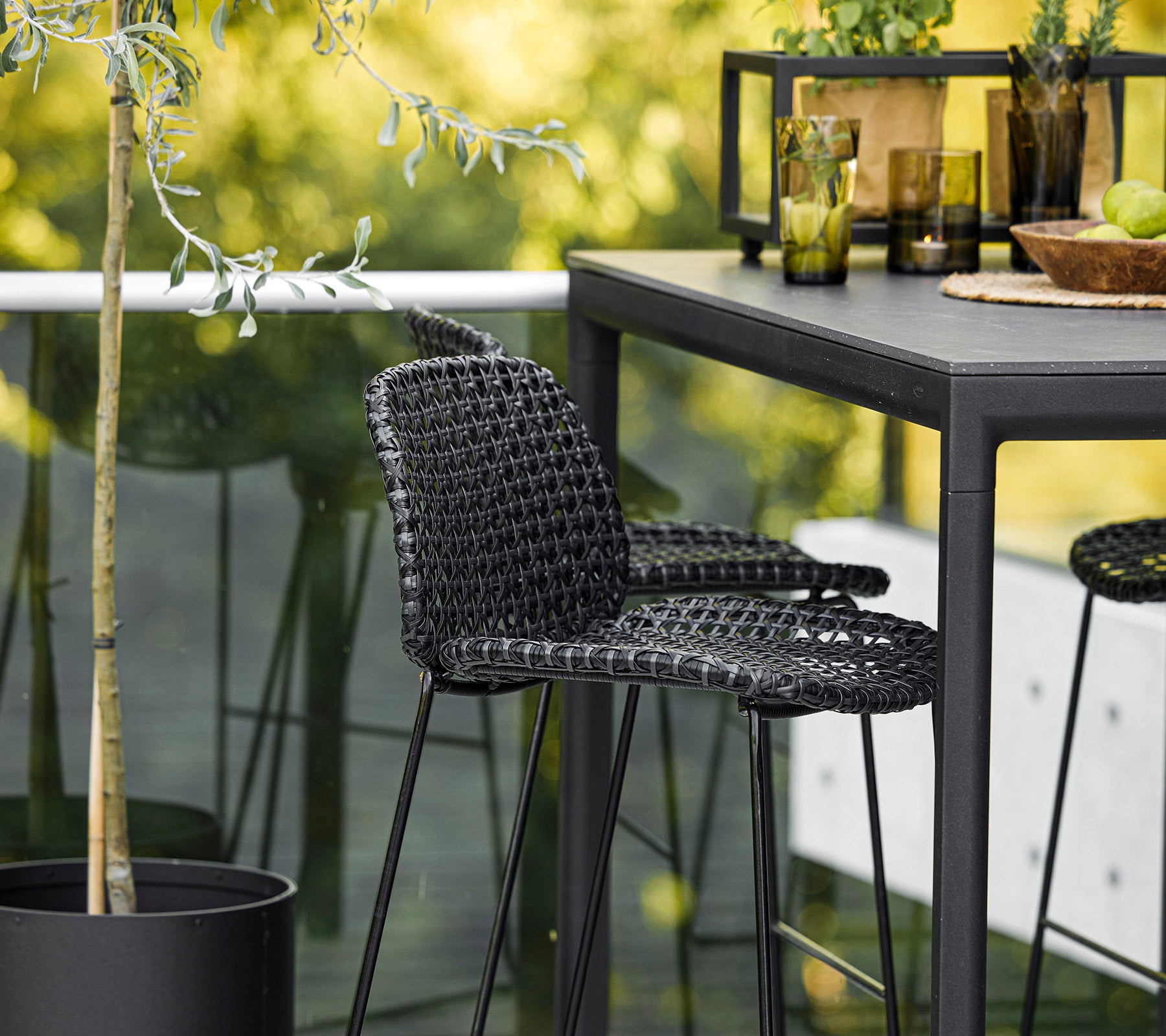 Une chaise tissée noire élégante associée à une table épurée, entourée de plantes décoratives et de verrerie, créant ainsi un cadre moderne.