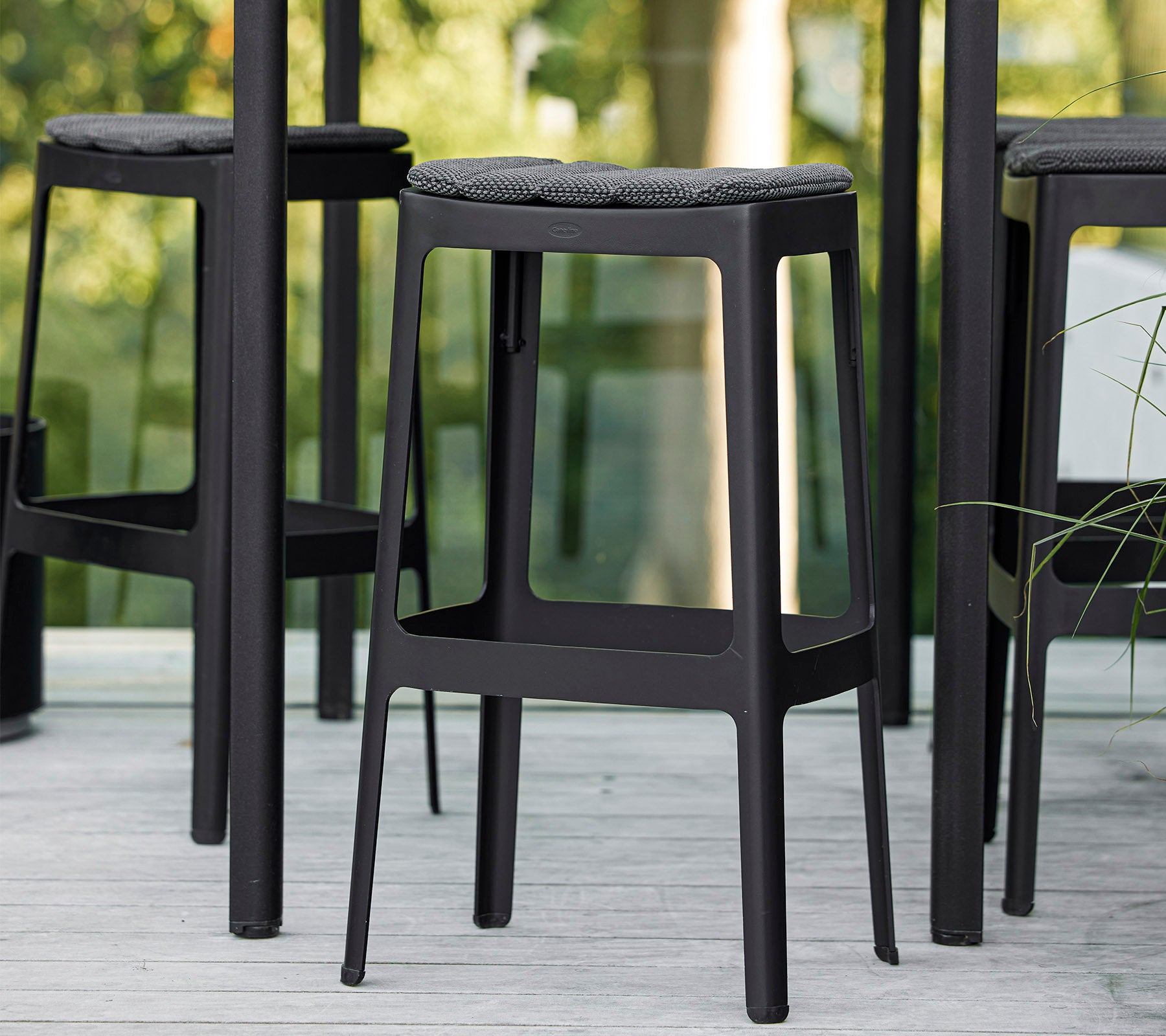 Tabourets de bar noirs au design minimaliste et aux sièges rembourrés, disposés très proches l'un de l'autre, mettant en valeur une esthétique moderne.