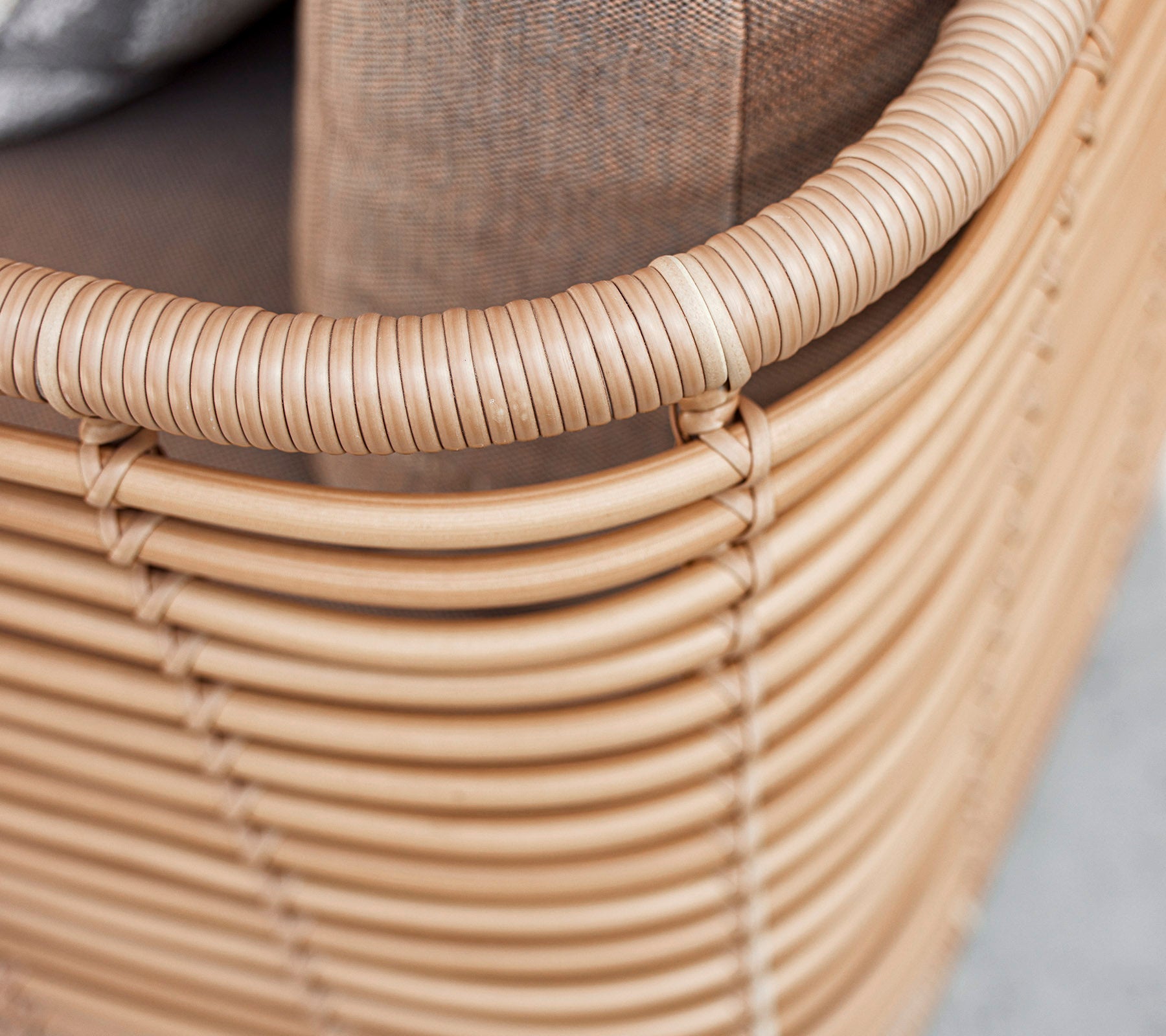 Siège tissé de couleur claire avec un bord arrondi et un coussin texturé, mettant en avant un design moderne et minimaliste.