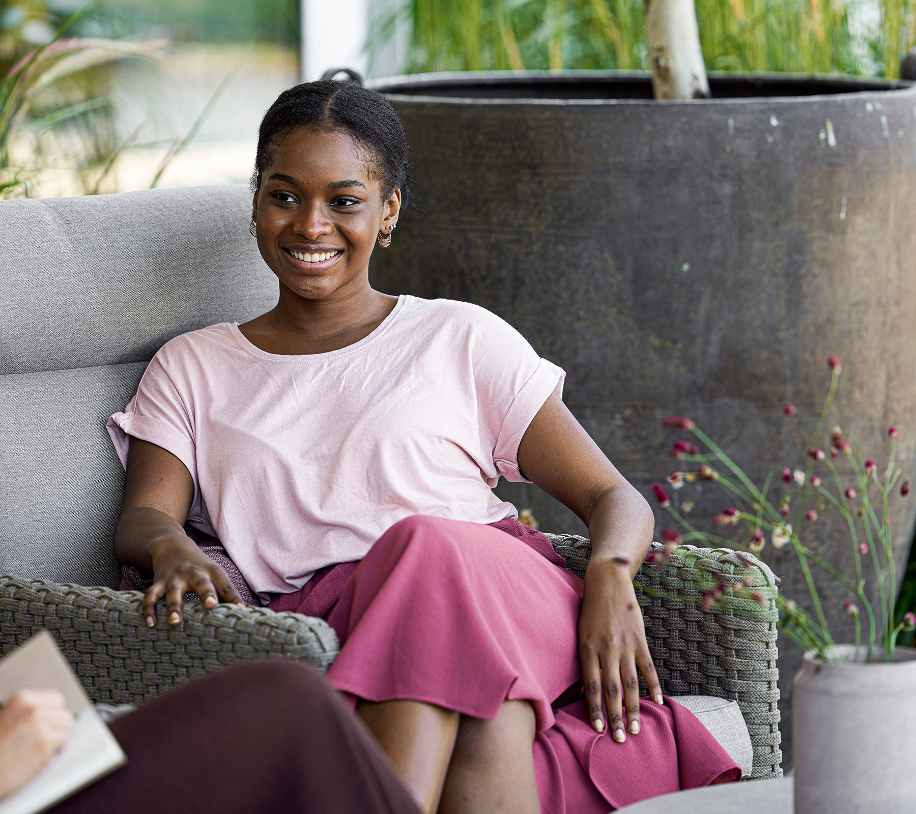 Une femme souriante en haut et jupe rose est assise confortablement sur un canapé, profitant d'un moment de détente dans un cadre serein.