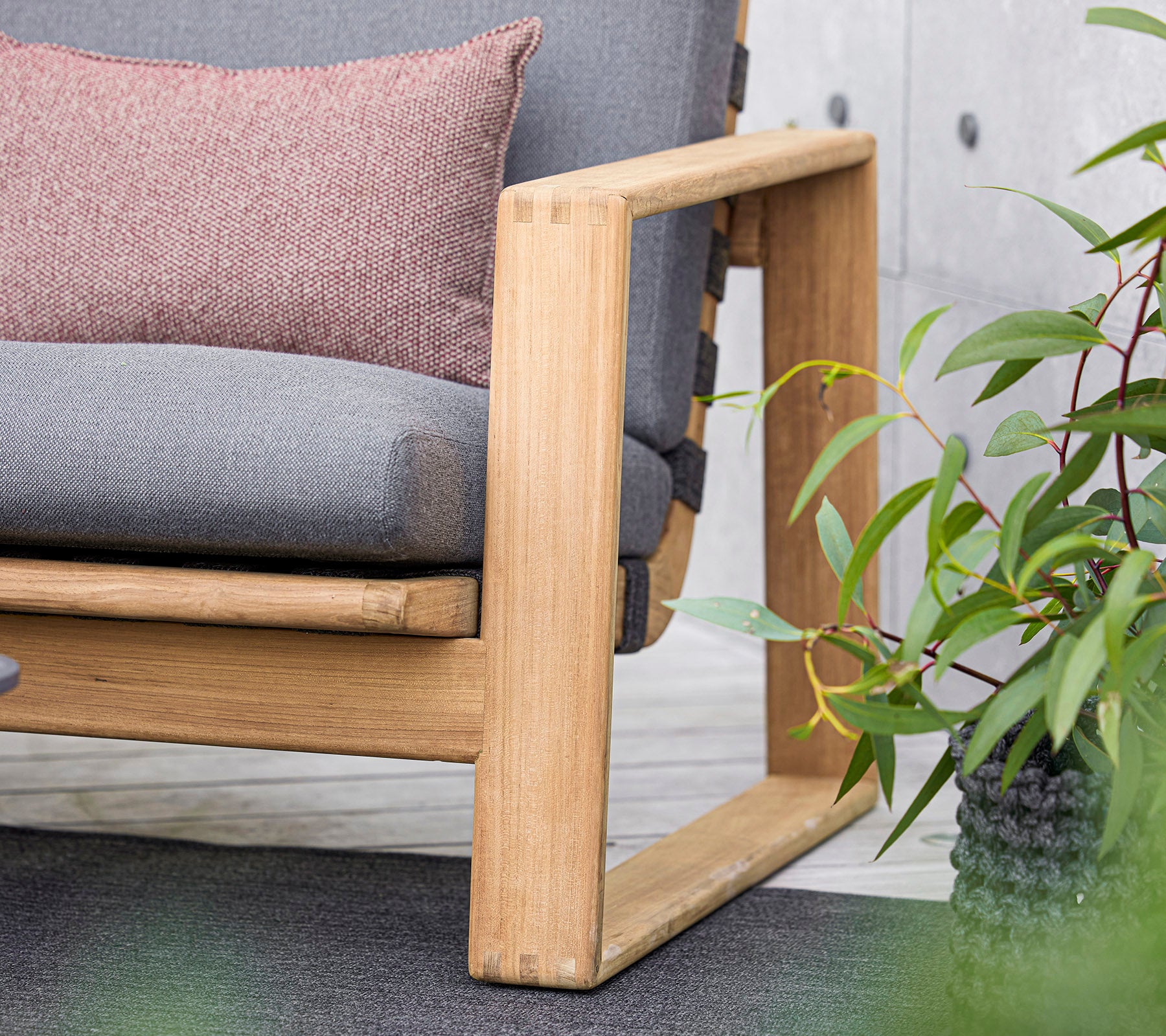 un canapé moderne avec un cadre en bois, doté de coussins gris et d'un coussin décoratif, complété par de luxuriantes plantes vertes à proximité.