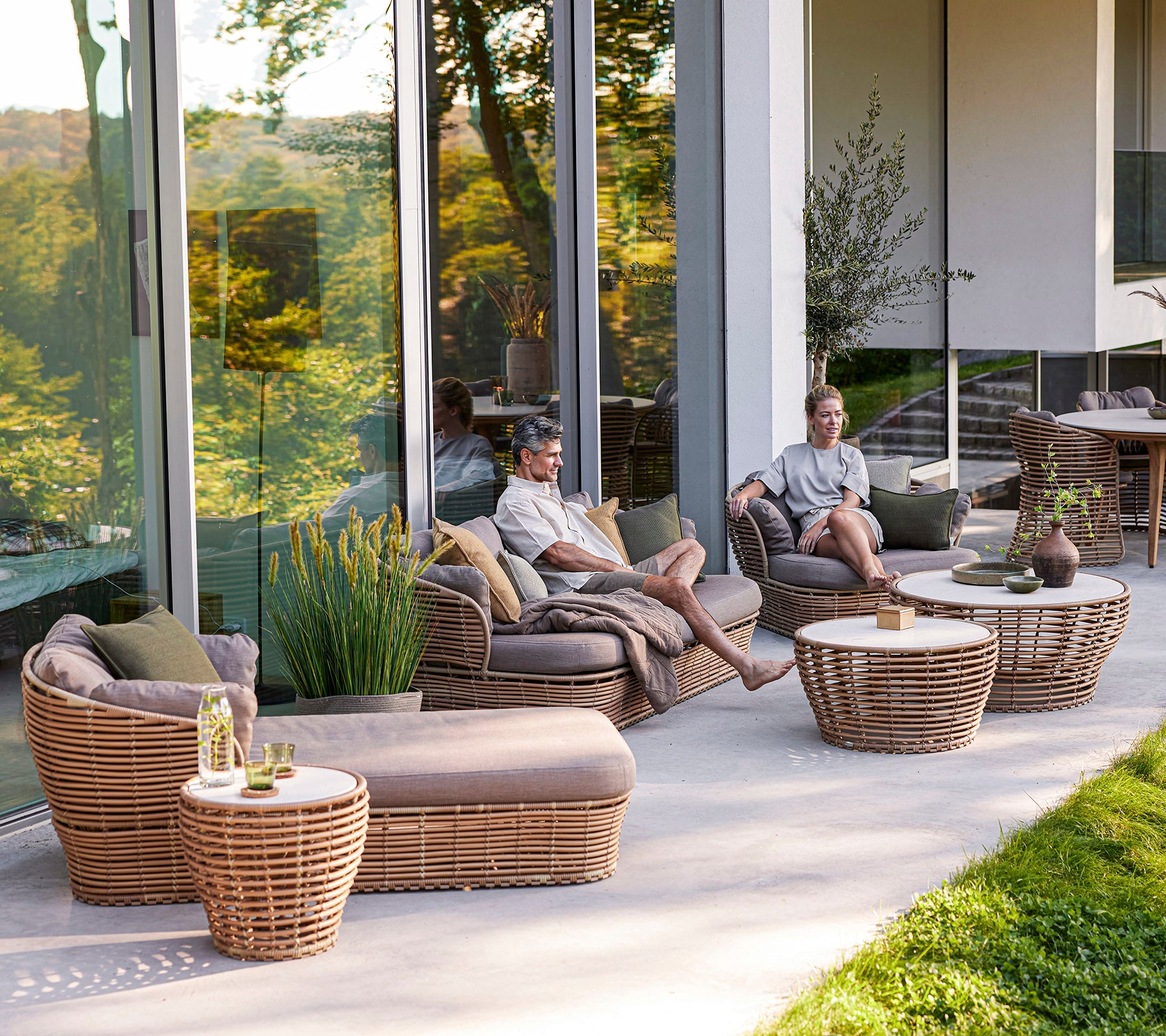Un espace de détente avec des meubles tressés, des coussins et des tables basses, où deux personnes profitent de leur temps ensemble.