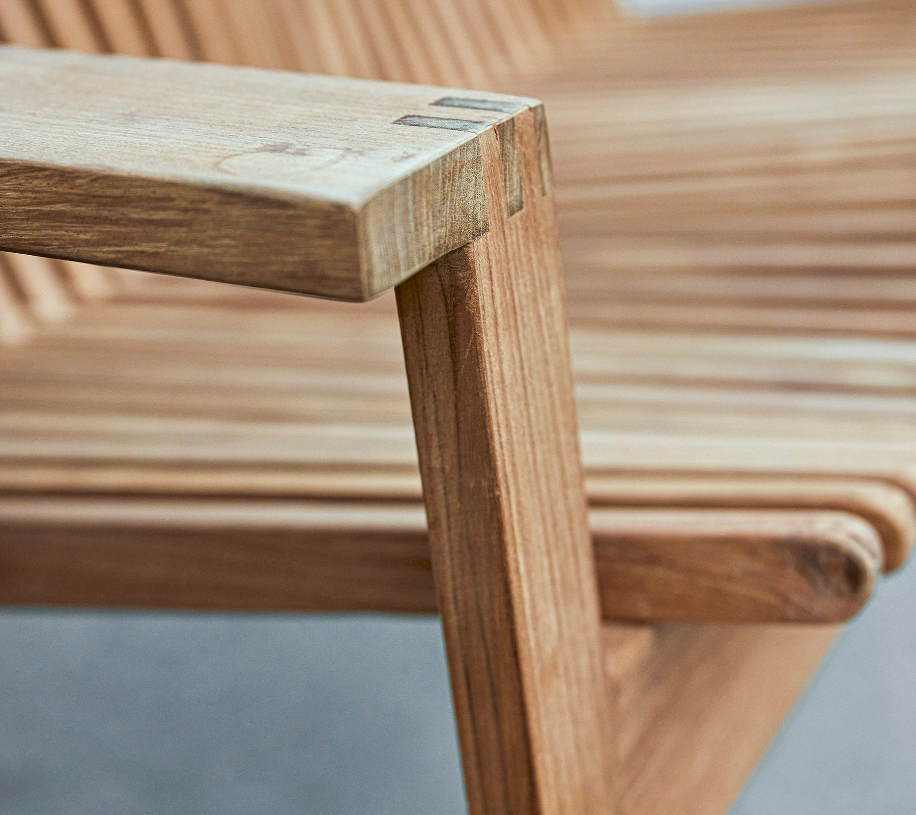 Gros plan d'un accoudoir de chaise en bois présentant un design épuré avec un siège à lattes et des finitions lisses.