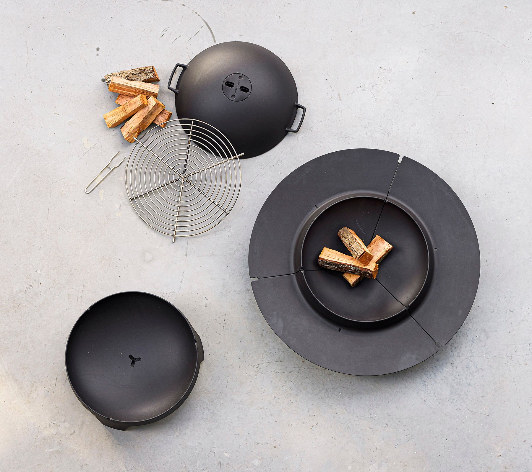 Un ensemble de cuisine noir comprenant un grill circulaire avec couvercle, une grille à griller et des morceaux de bois disposés à proximité.