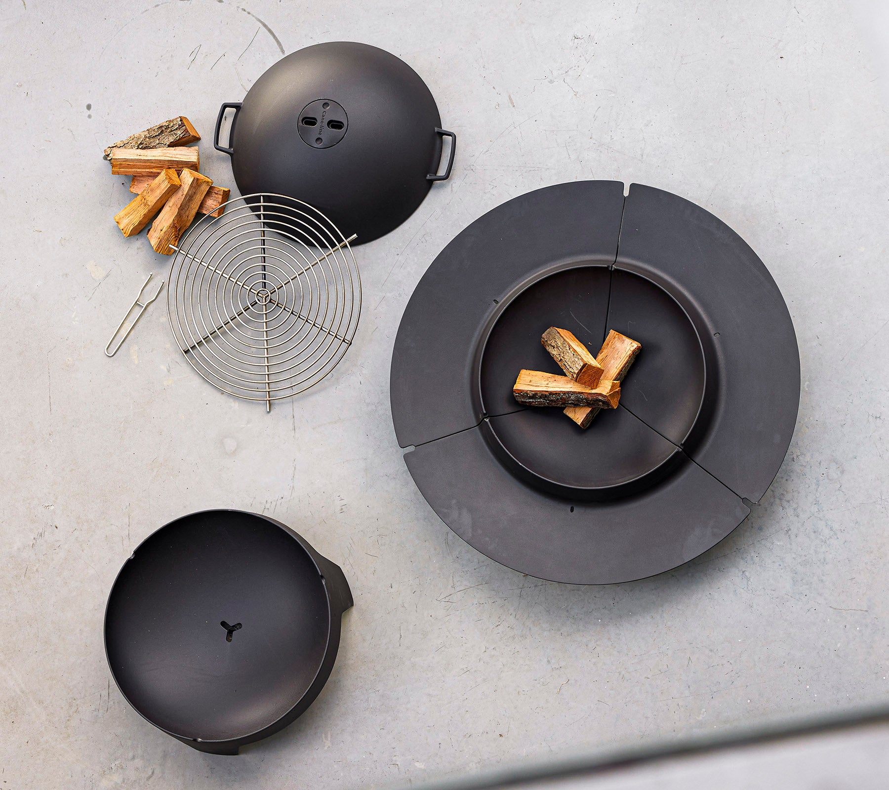 Équipement de cuisson noir disposé avec du bois de chauffage et une grille en fil métallique, conçu pour le barbecue en plein air et la cuisson au feu.