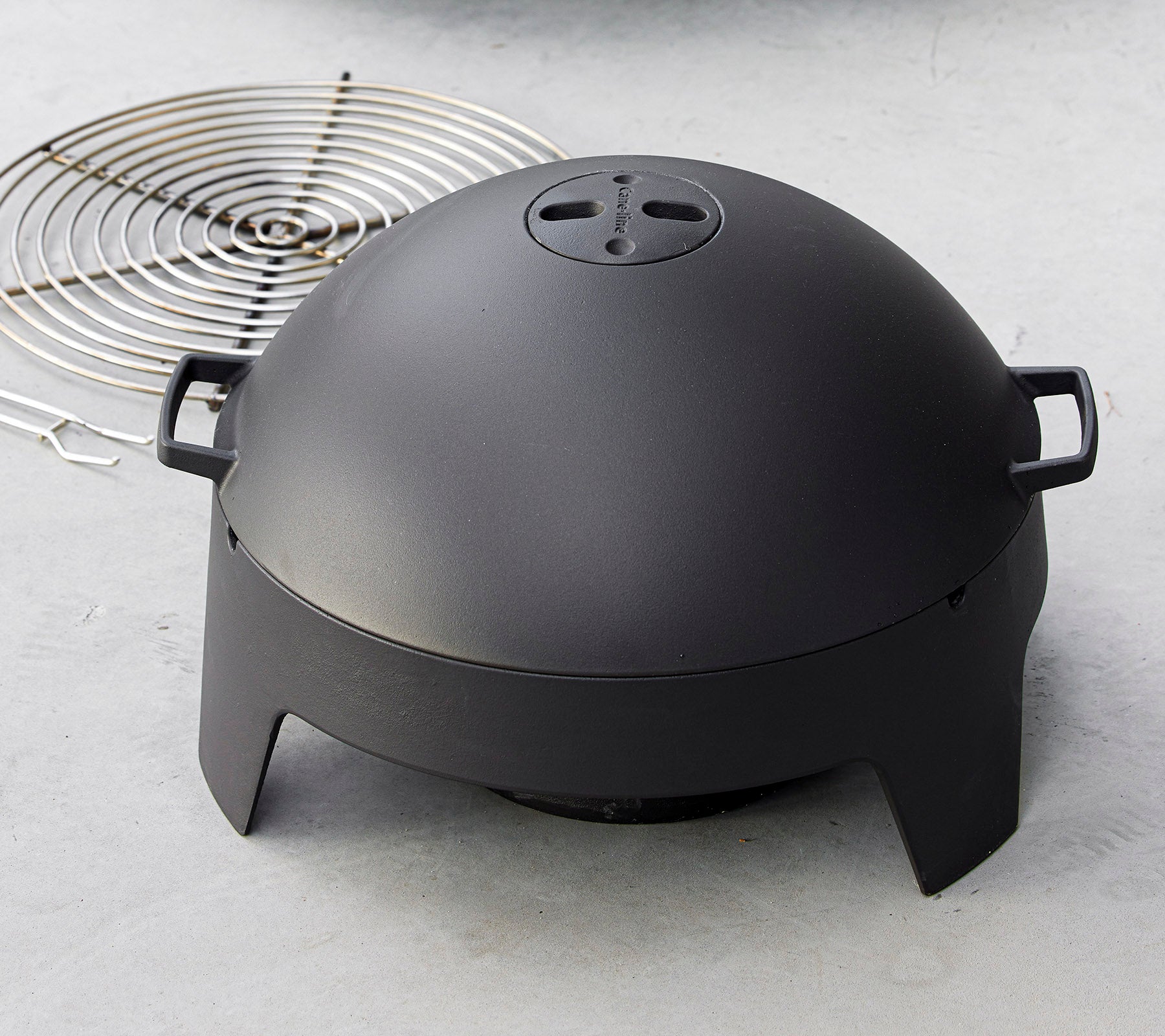 Un appareil de cuisson noir élégant en forme de dôme avec des poignées, accompagné d'une grille circulaire. Idéal pour griller et cuisiner en extérieur.