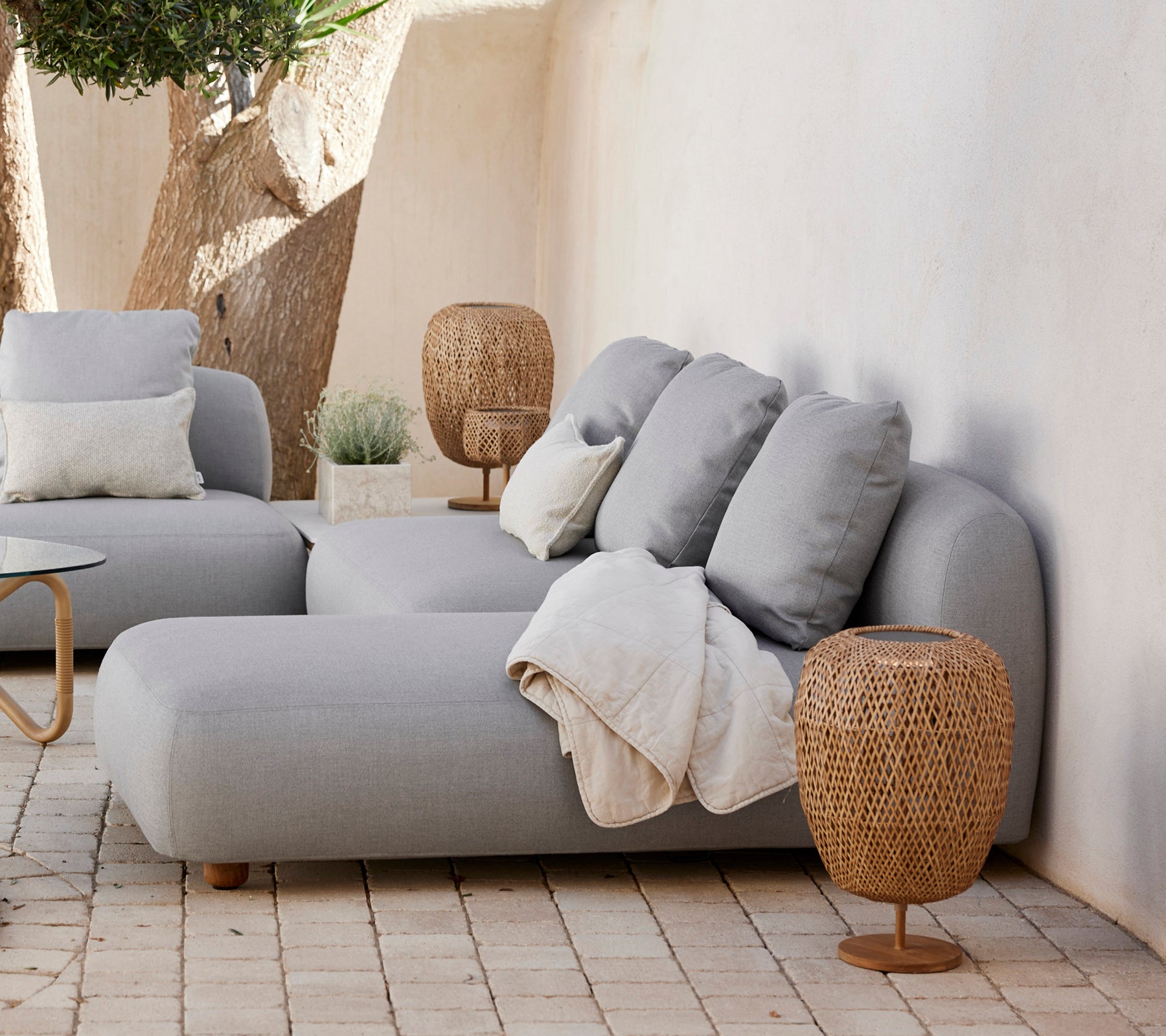 Sofa gris moderne avec des coussins et une table d'appoint tissée dans un cadre de salon minimaliste.
