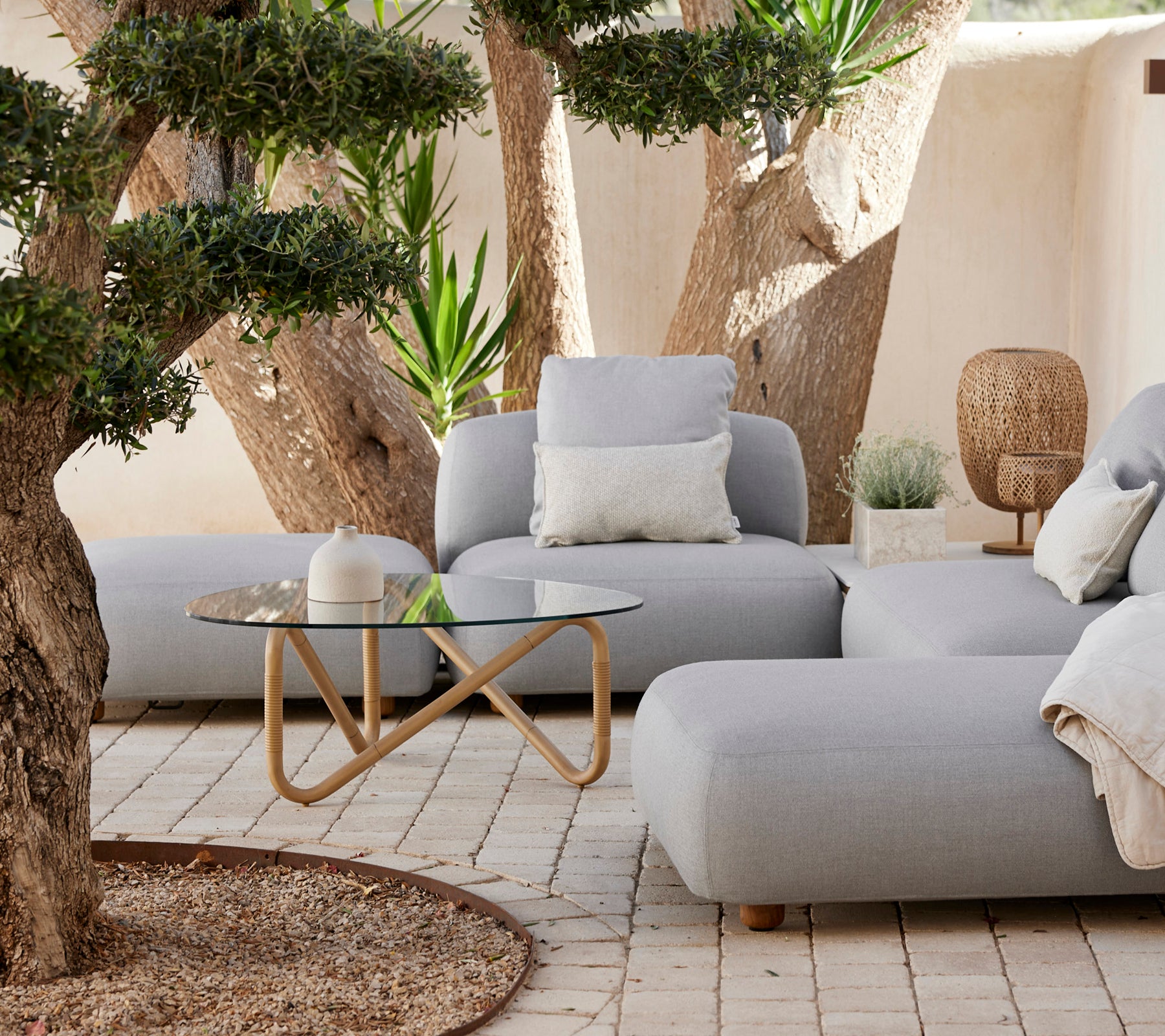 Espace lounge moderne avec un canapé gris, un coussin blanc et une table basse en verre.