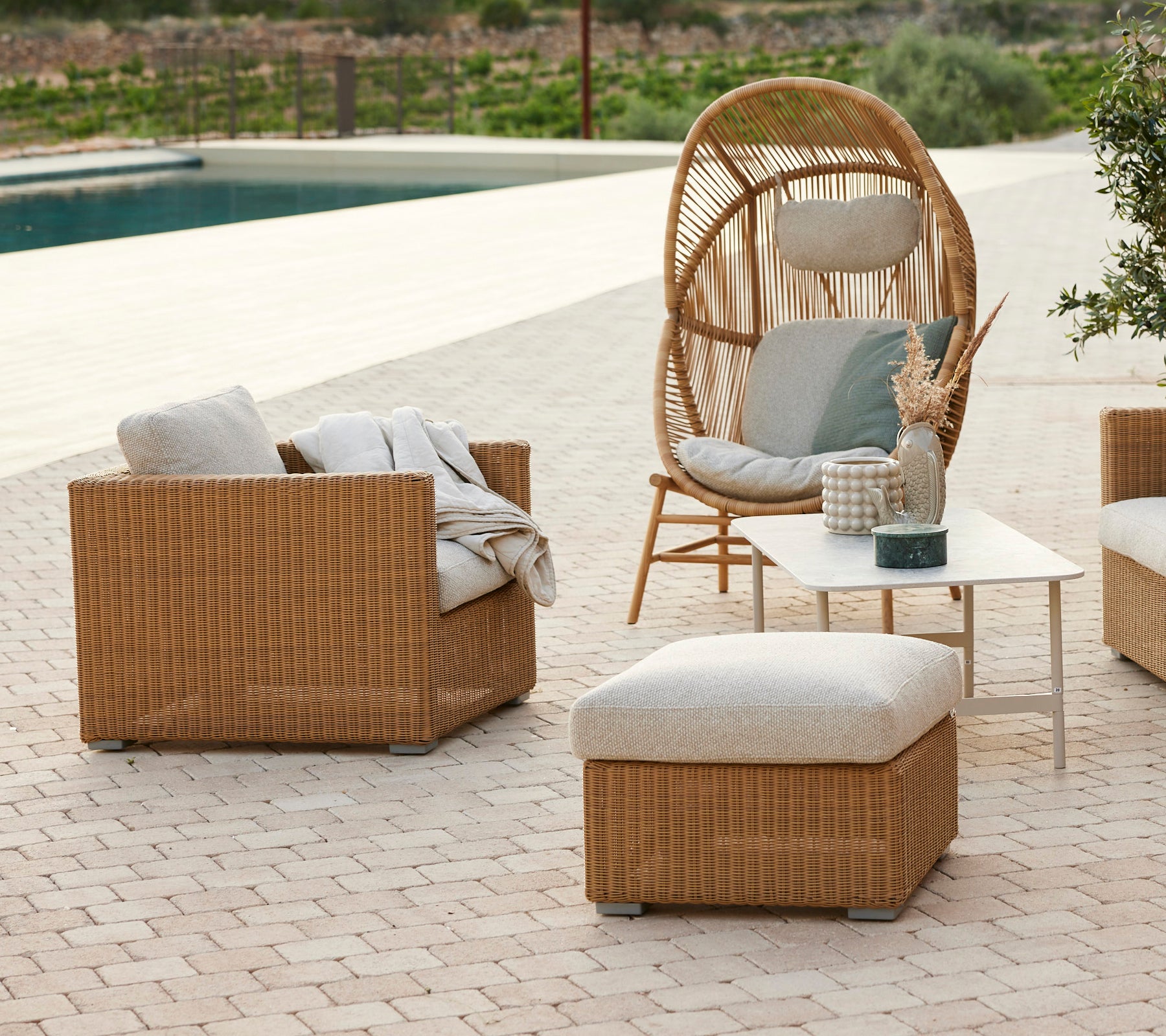 Espace lounge moderne avec une chaise en rotin, des coussins gris, un canapé en rotin et une table basse.