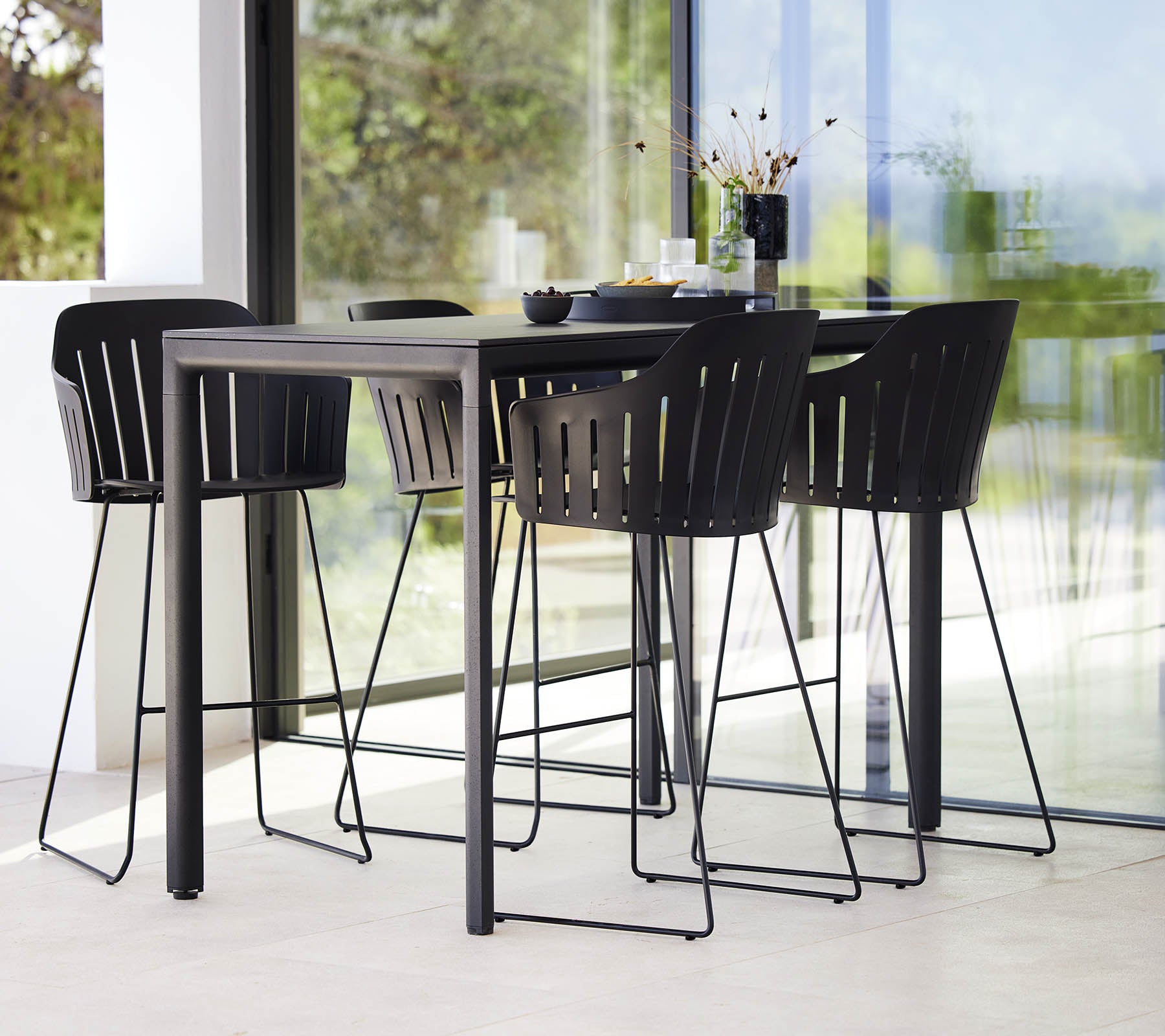 Une table de bar noire élégante associée à des chaises de bar modernes avec un design à lamelles, créant un agencement de sièges élégant.