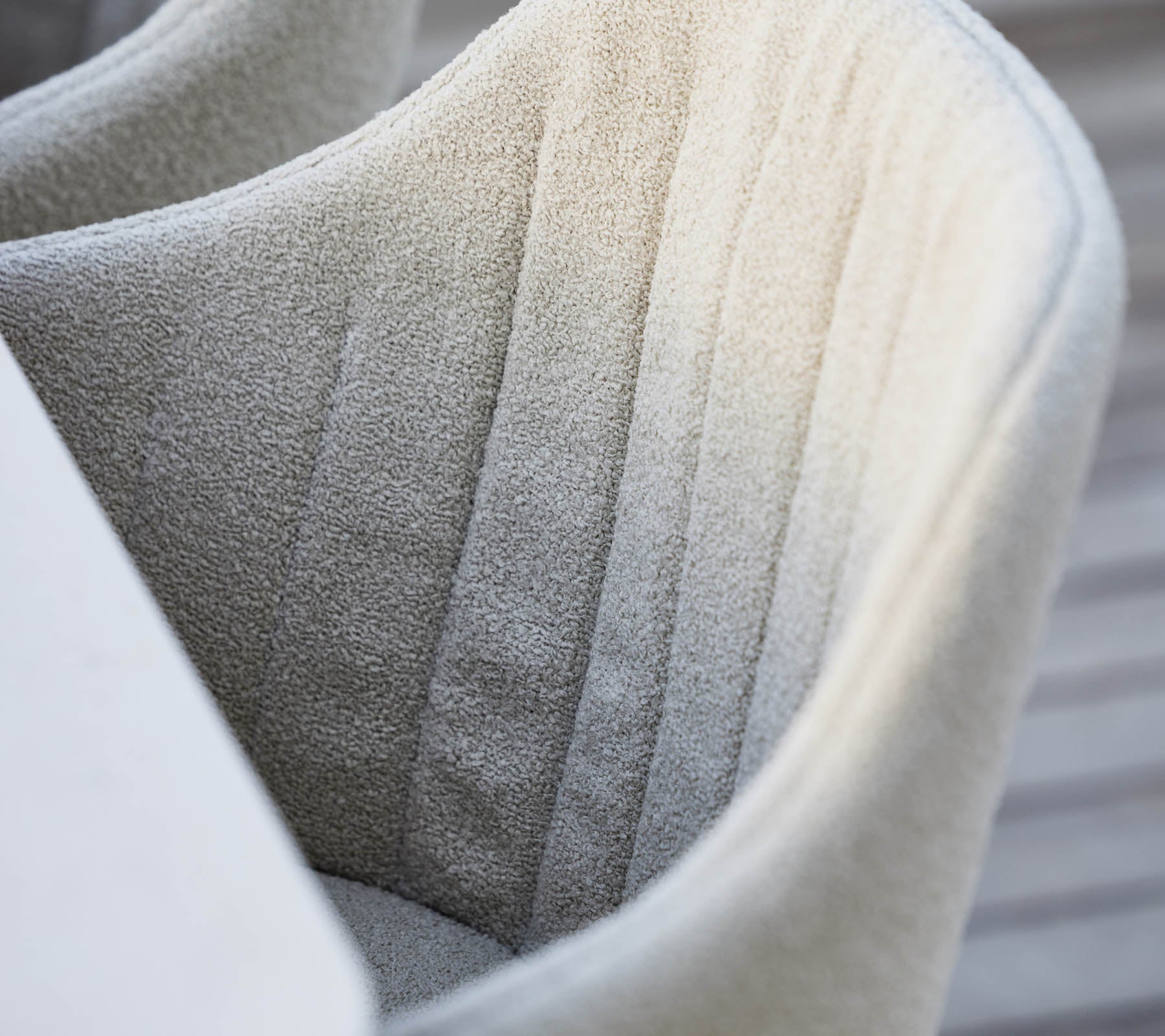 Chaise texturée, entièrement rembourrée avec une couture verticale subtile, présentant une couleur douce et neutre et une esthétique de design moderne.