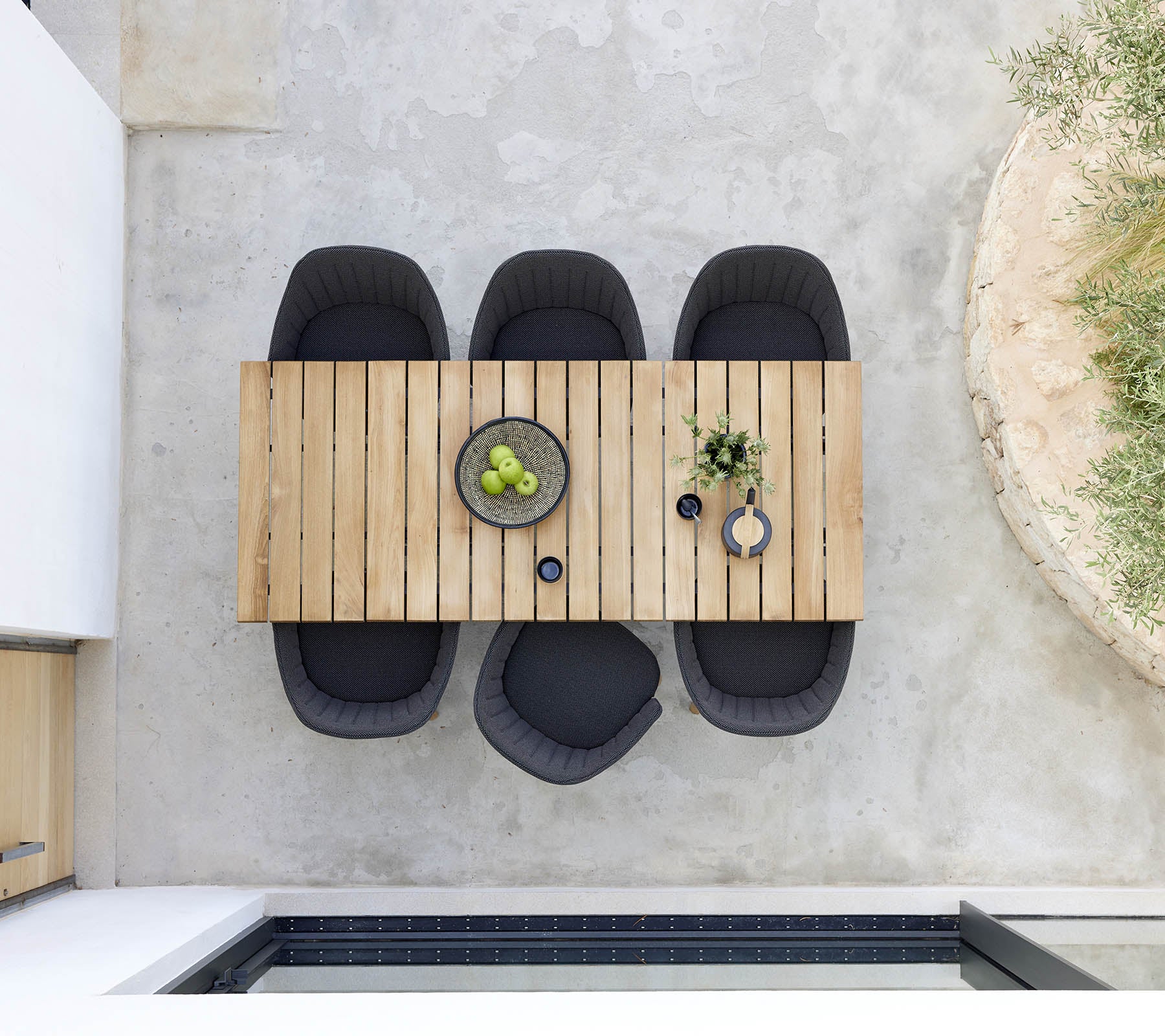 Table à manger en bois élégante accompagnée de quatre chaises noires, avec un bol de fruits verts et des plantes décoratives pour une touche moderne.