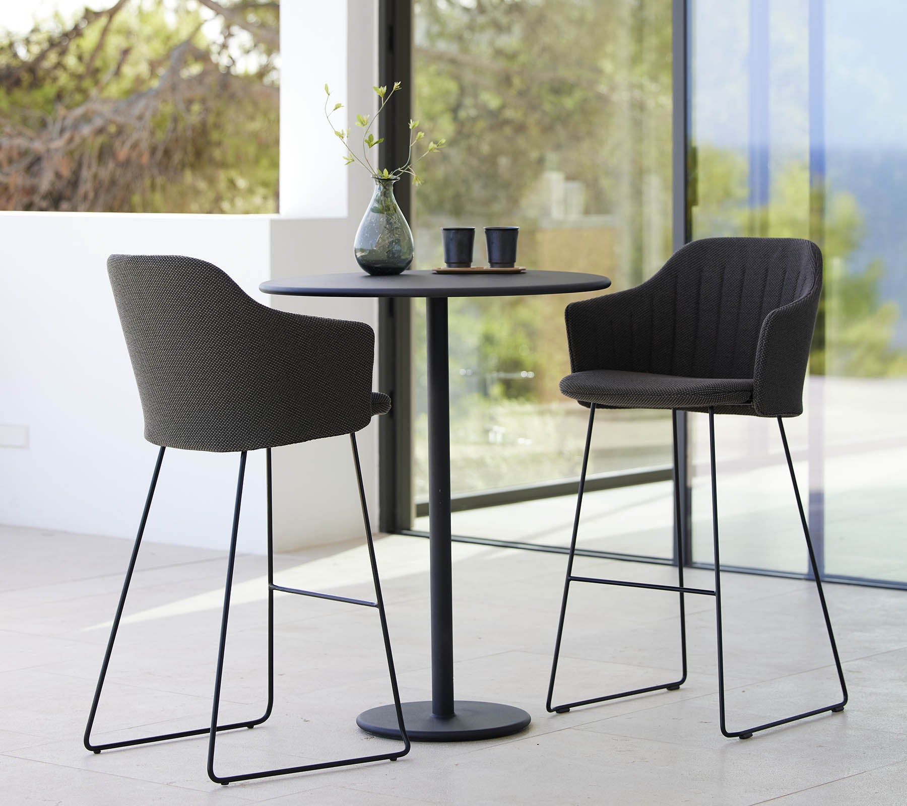 Deux chaises élégantes associées à une table de bar épurée, complétées par un vase et des tasses, créant un agencement de sièges moderne et accueillant.