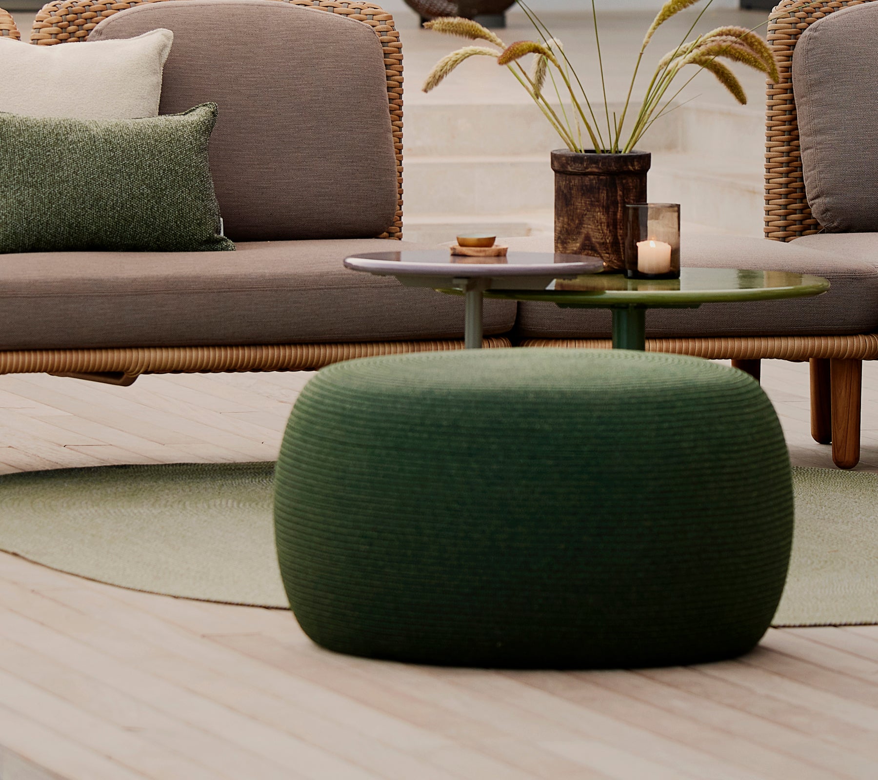 Grand repose-pieds rond vert avec une surface texturée, accompagné d'une petite table et d'éléments décoratifs.
