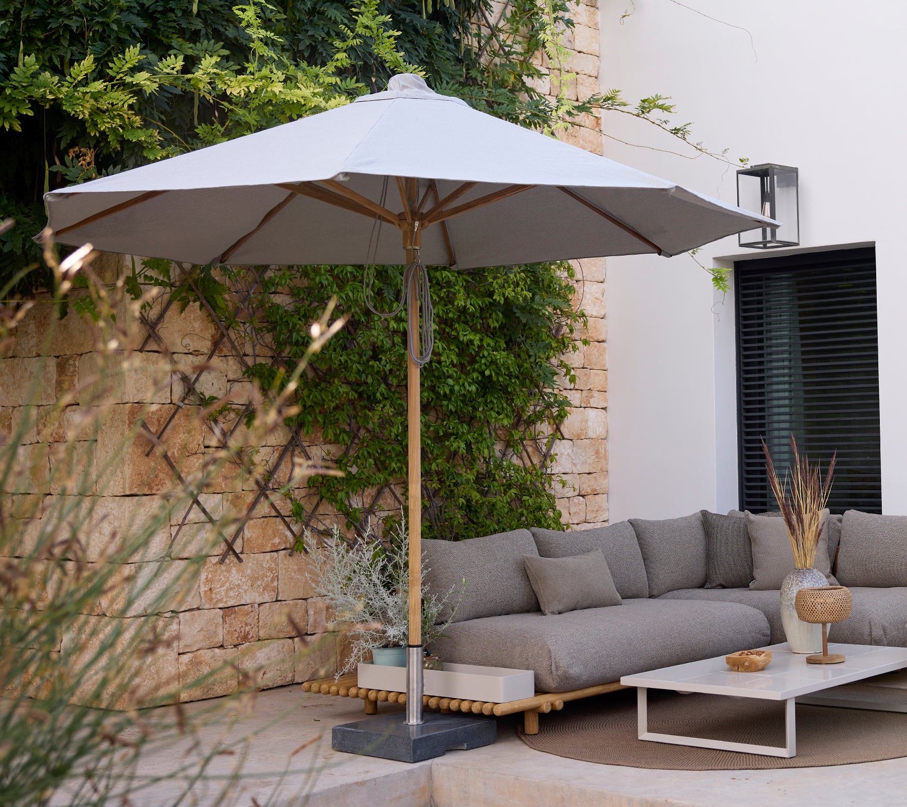 Espace lounge moderne avec un canapé gris, une table blanche et un parasol gris.