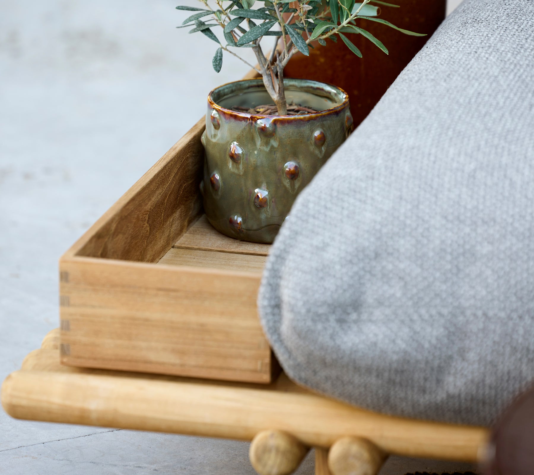 Plateau en bois avec coussin gris et pot vert contenant une plante.