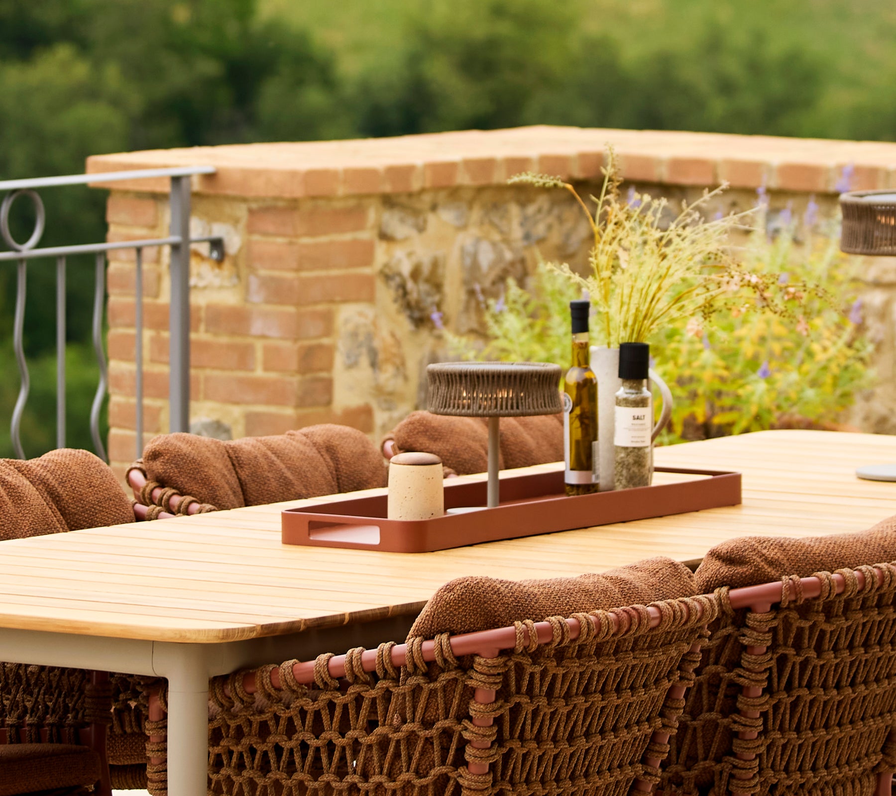 Un grand plateau rouge rectangulaire est posé sur une table, avec de l'huile d'olive, une bougie et des éléments décoratifs, entouré de sièges chauds et texturés.