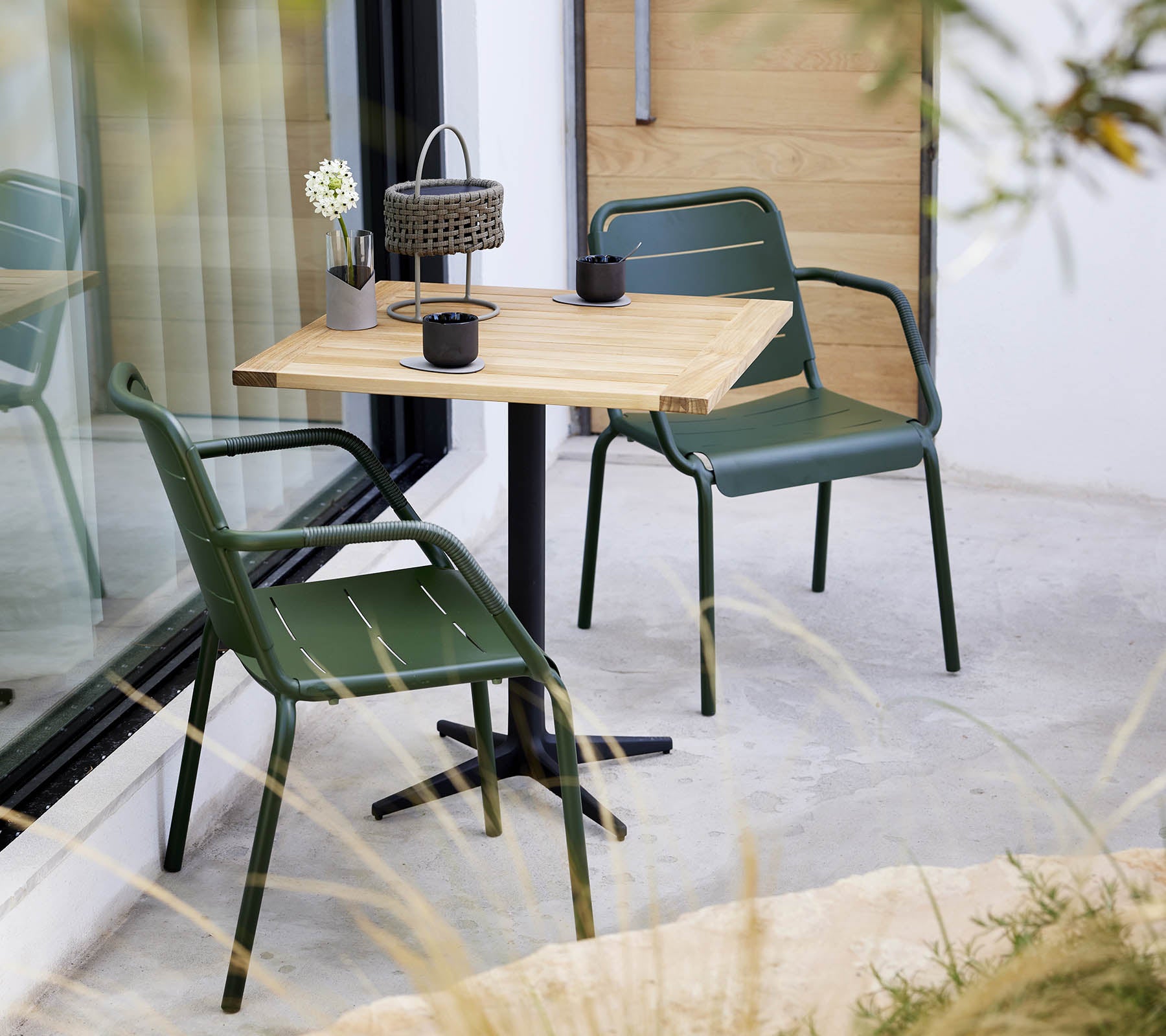 Un cadre minimaliste avec une table en bois et des chaises vertes, avec un petit arrangement floral et une lanterne décorative.