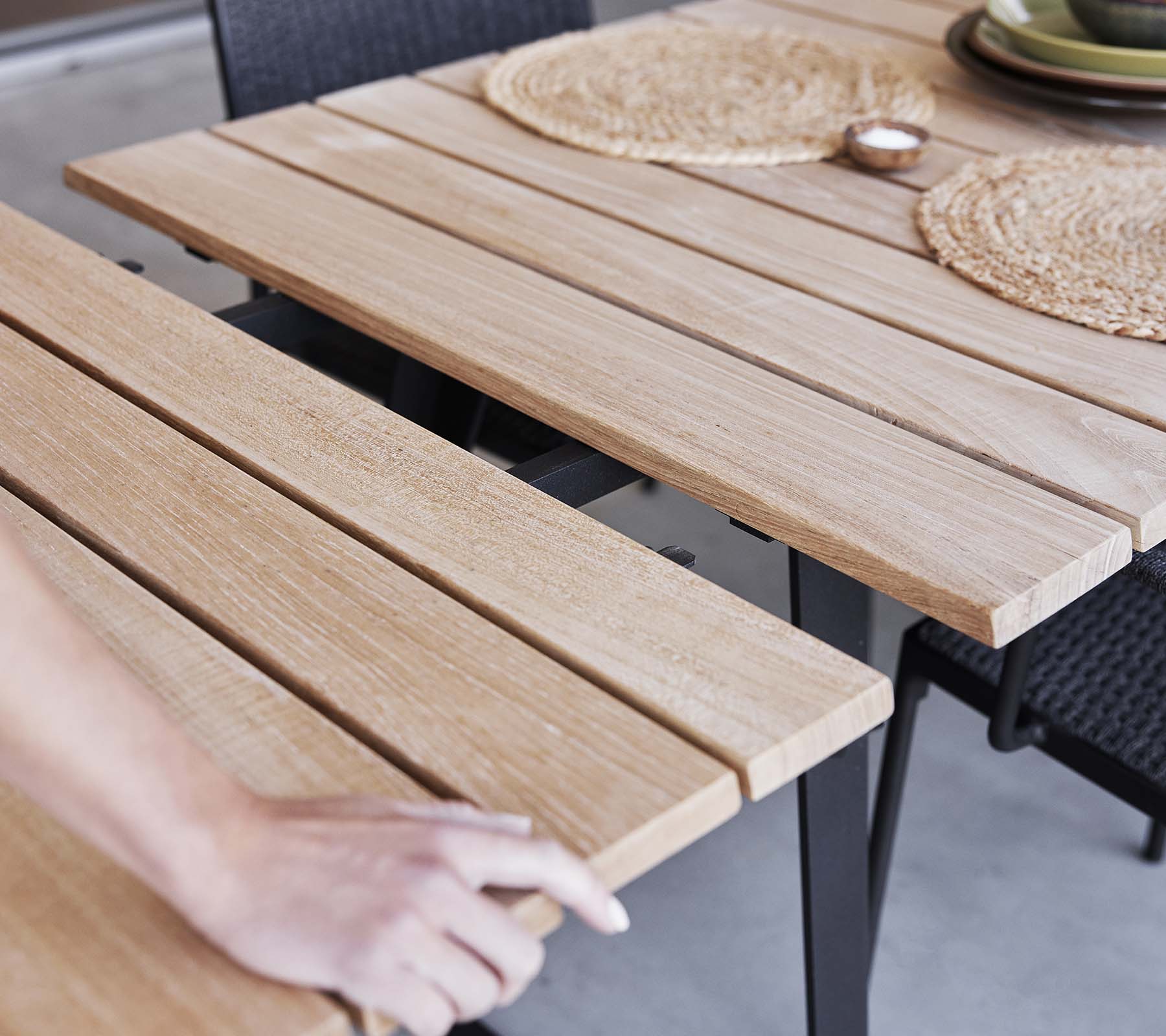 Détail d'une table en bois avec un design à lattes, des sets de table et une esthétique minimaliste, parfaite pour les repas ou les rassemblements.