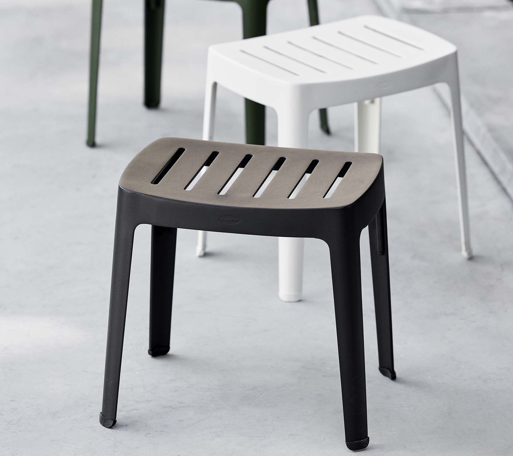 Tabouret élégant en noir avec dessus à lattes, affichant un design moderne ; complété par un tabouret blanc à l'arrière-plan.
