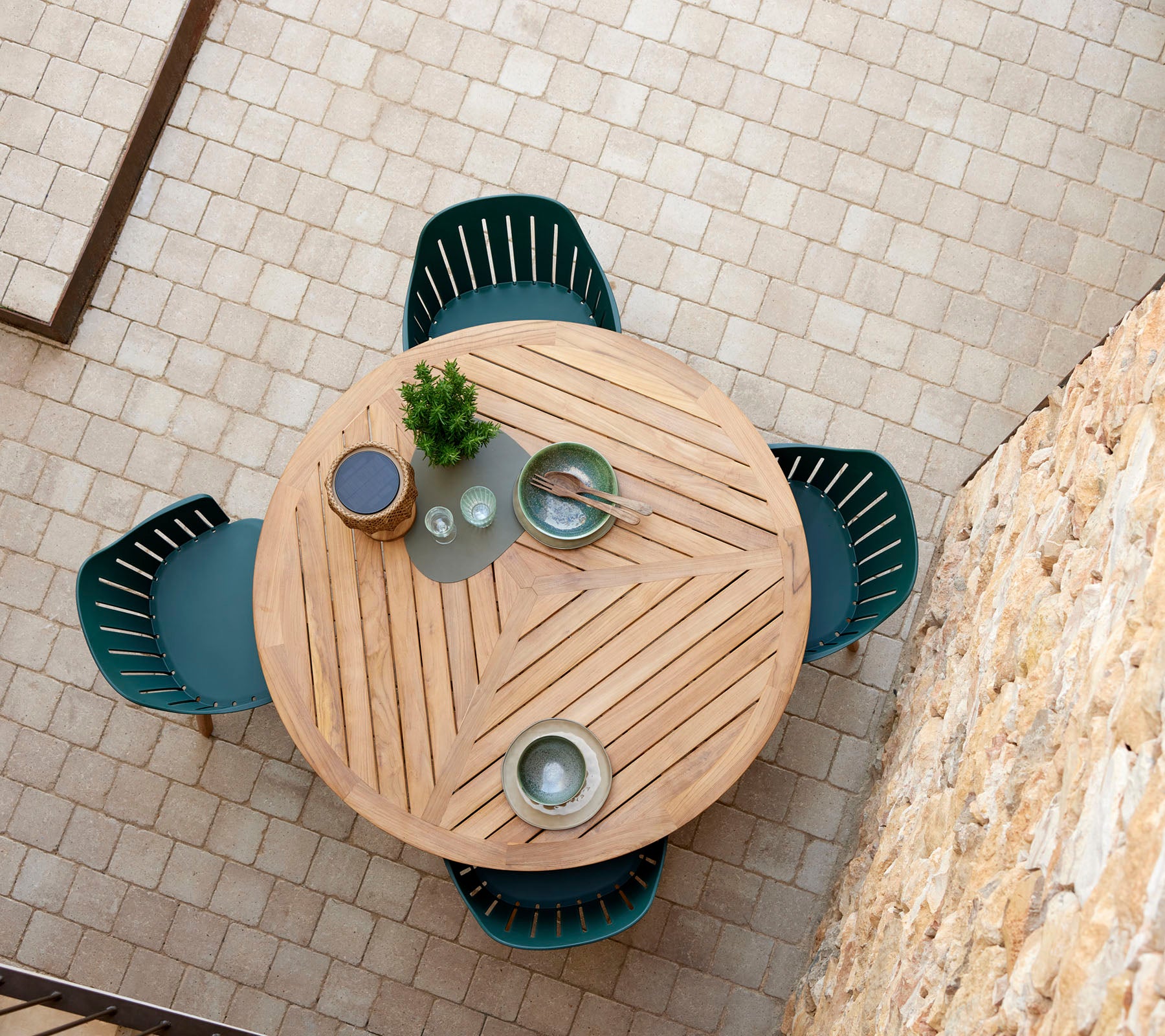 Une table ronde en bois avec un motif en chevrons, entourée de quatre chaises vertes, et ornée de plats décoratifs et d'une petite plante.