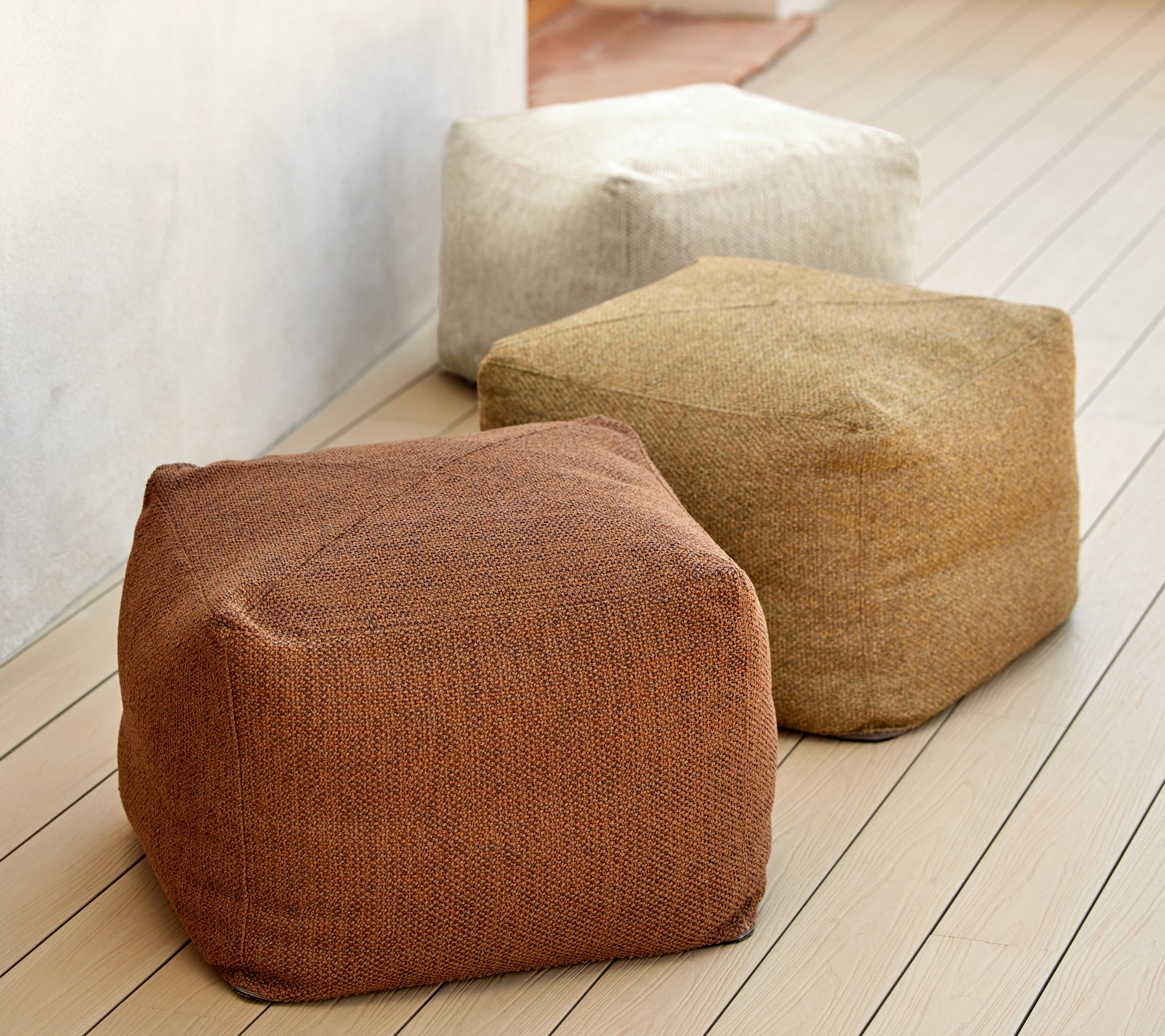 Trois poufs texturés dans des tons terreux de brun, beige et tan, exposés sur une surface en bois. Idéal pour des sièges et une décoration polyvalents.