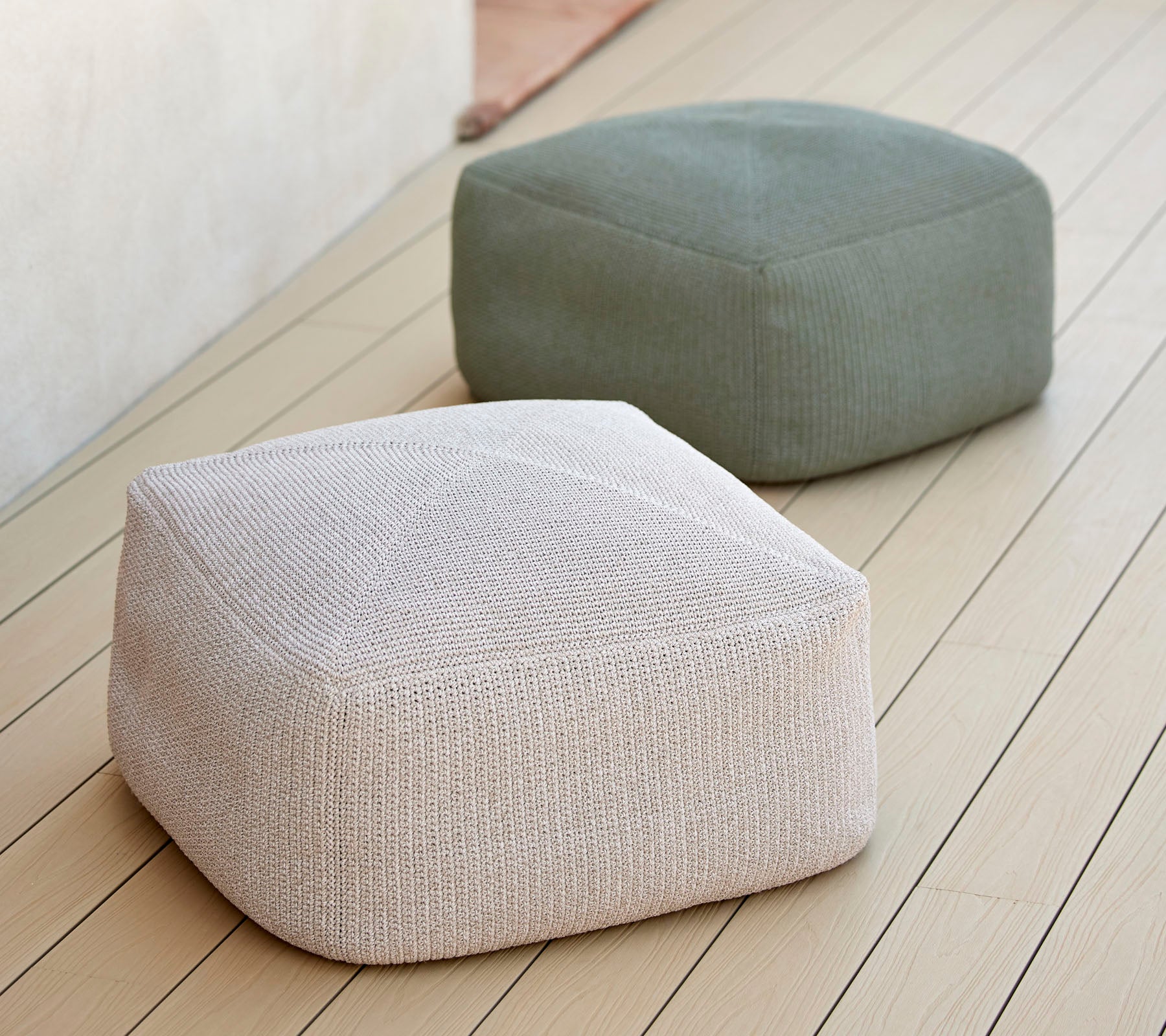 Deux poufs élégants et texturés dans des tons neutres, un blanc et un vert, disposés sur une surface lisse, idéaux pour un siège polyvalent.