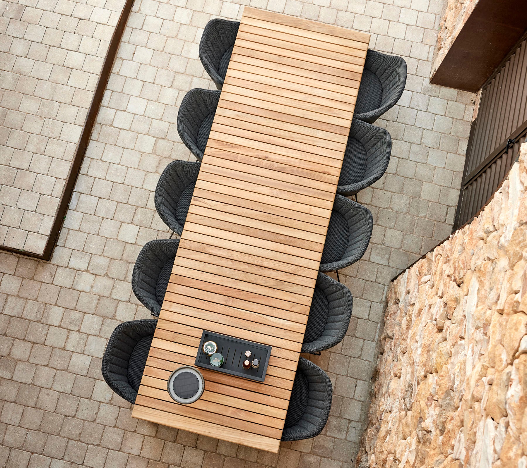 Une longue table en bois au design à lattes, entourée de chaises noires rondes, avec un petit plateau contenant des tasses au sommet.