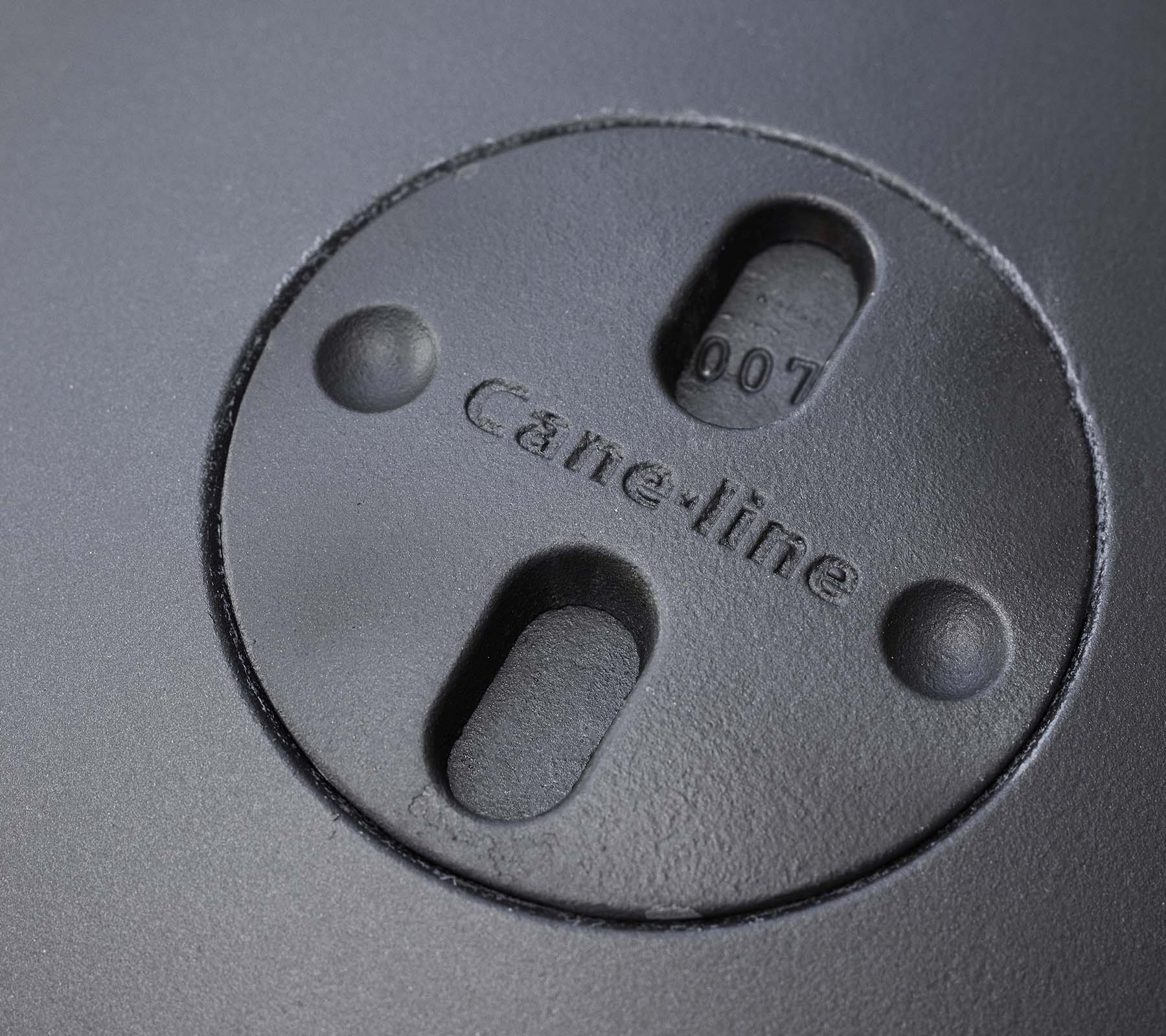 Gros plan d'une caractéristique circulaire avec le logo "Cane-line" gravé et deux fentes, faisant partie d'un design de foyer.