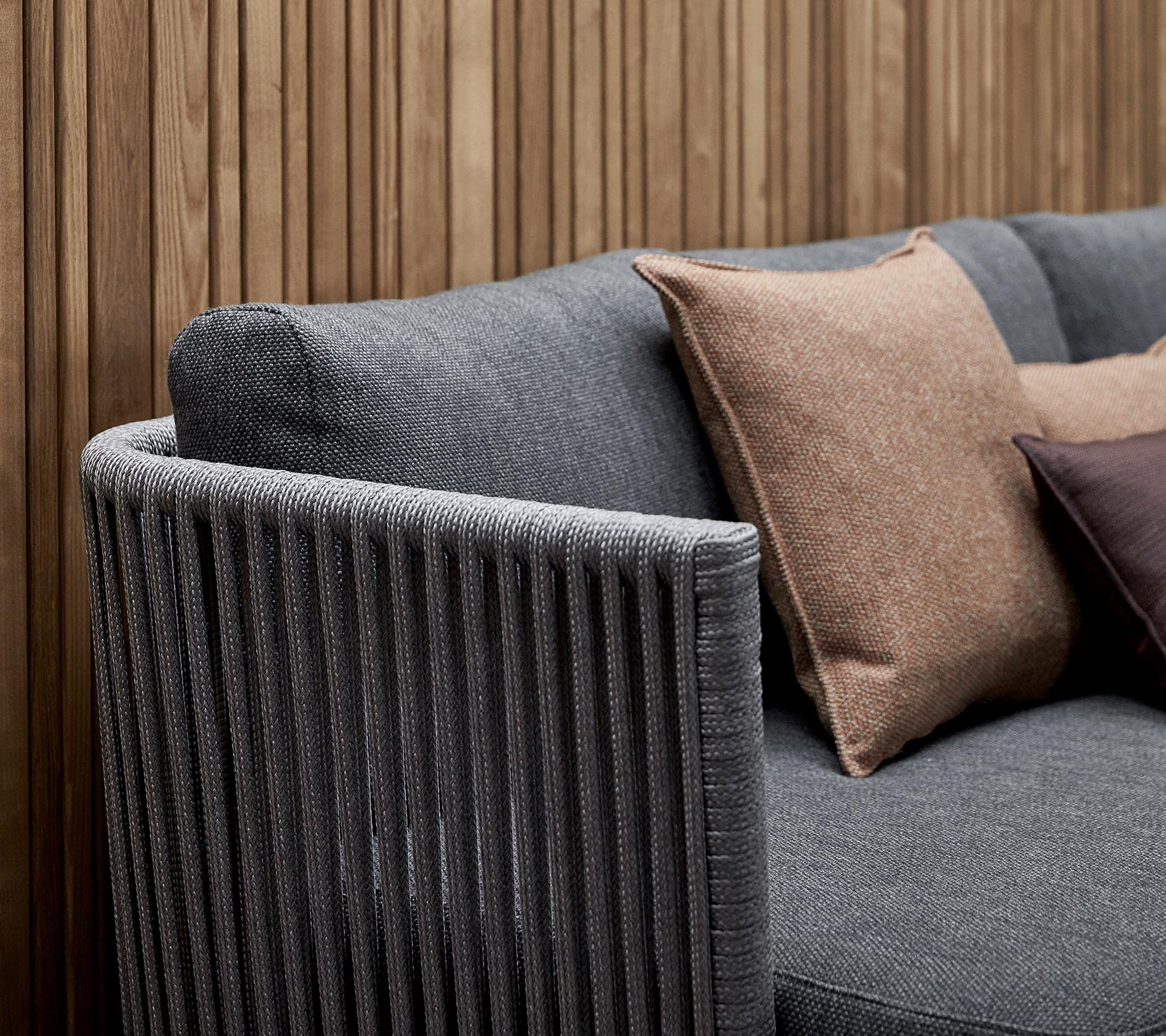 Canapé élégant en tissu gris texturé avec des coussins décoratifs aux teintes terreuses et un design de repose-bras à rayures verticales.