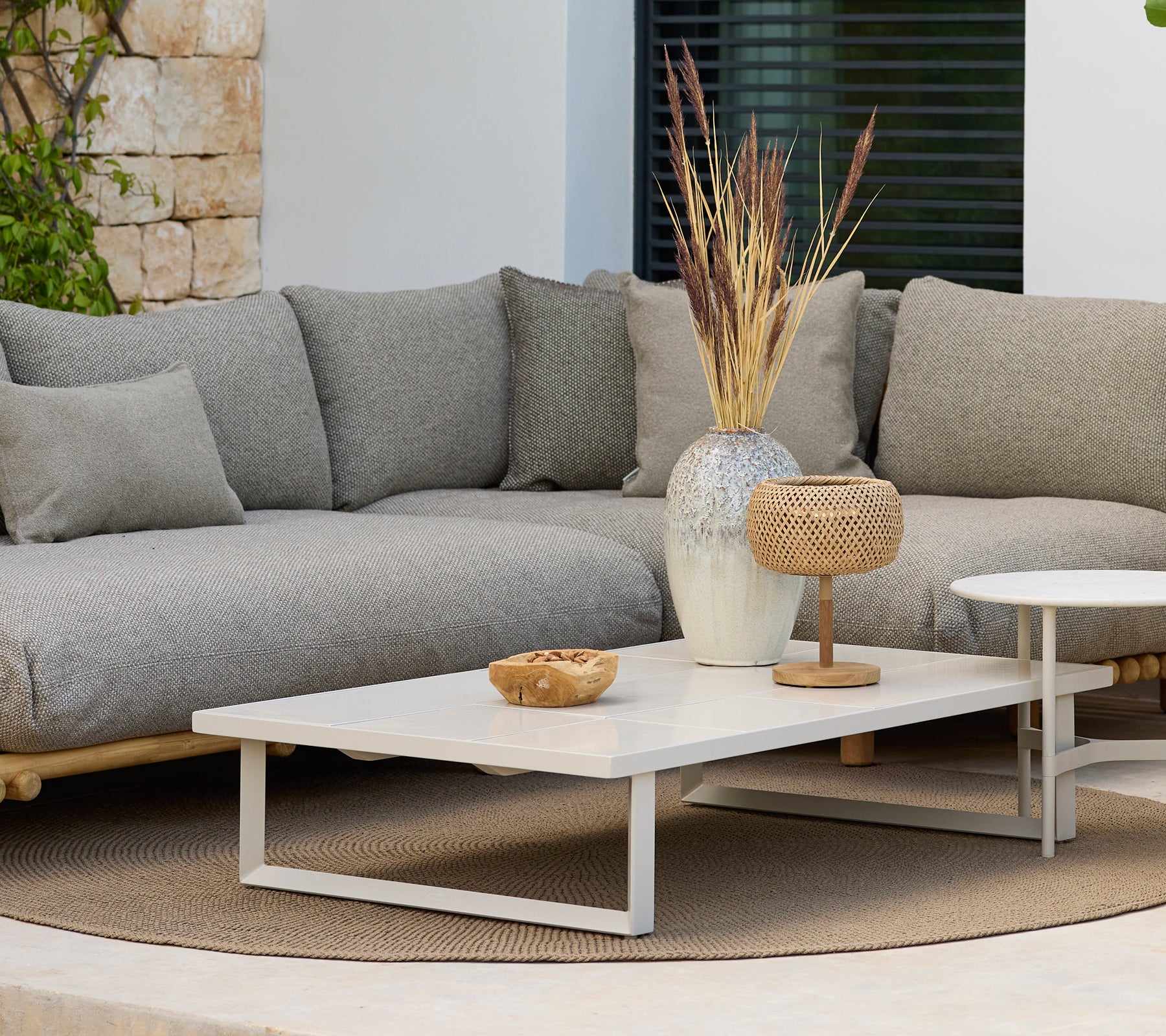 Espace lounge moderne avec un canapé gris et une table basse blanche avec décoration.