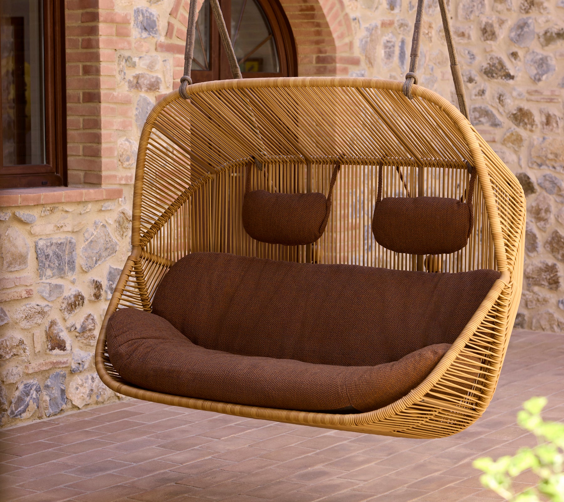 Sofa suspendue 2 places avec un cadre en rotin tressé et des coussins marron, offrant un coin confortable pour se détendre.