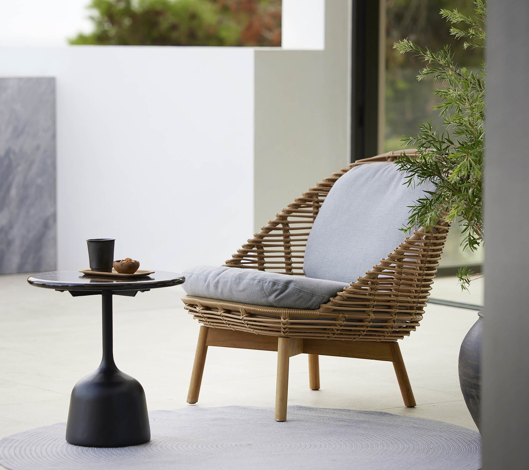 Un fauteuil lounge élégant avec un design tressé et des coussins doux, accompagné d'une table d'appoint épurée et d'une petite plante. Idéal pour se détendre.