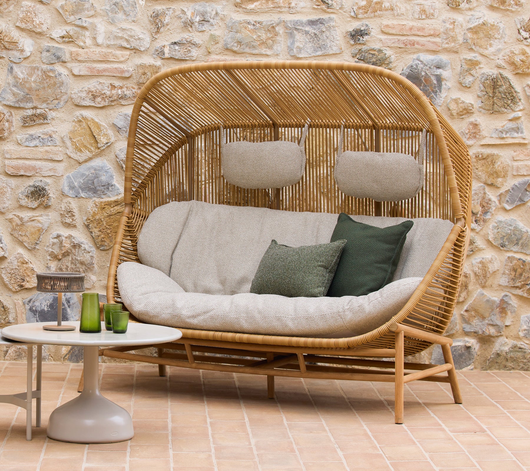 Canapé Hive avec des coussins moelleux et des accents verts aux côtés des tables basses Glaze, sur fond de pierre naturelle.