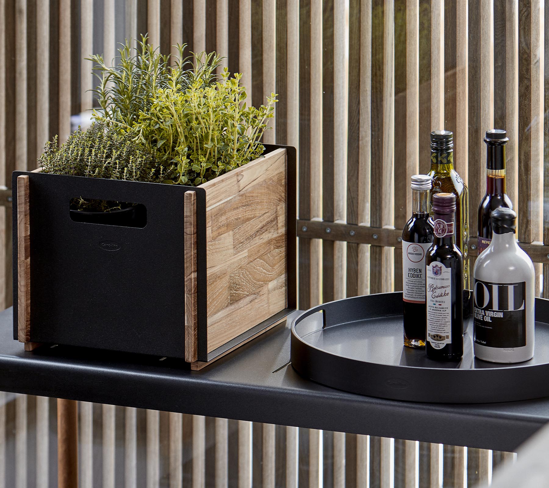 Un pot en bois avec des plantes à côté d'un plateau circulaire noir contenant plusieurs bouteilles d'huile et de vinaigre.