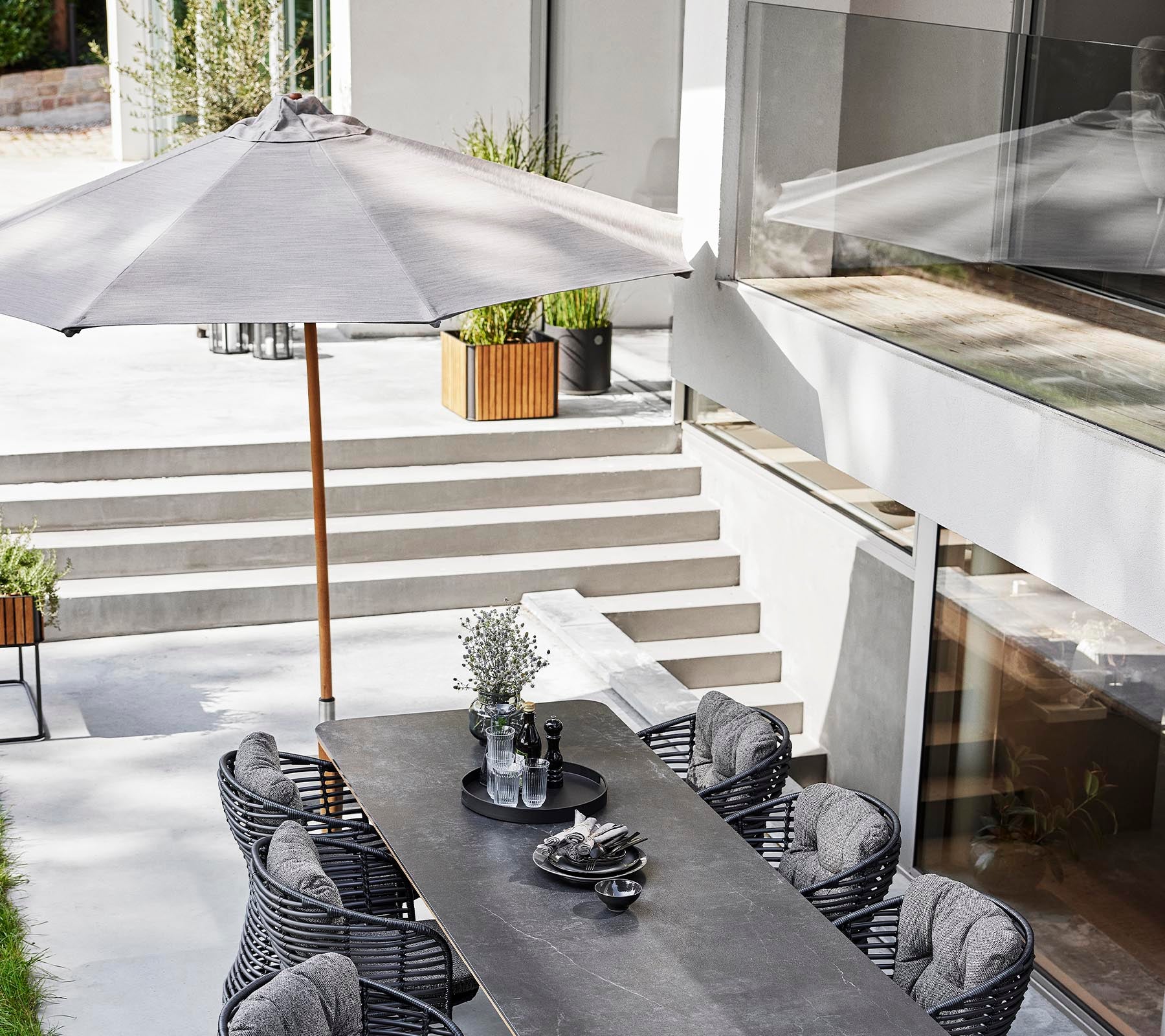 Un ensemble de repas en plein air élégant avec une longue table, des chaises en osier et un parasol classique pour l'ombre.