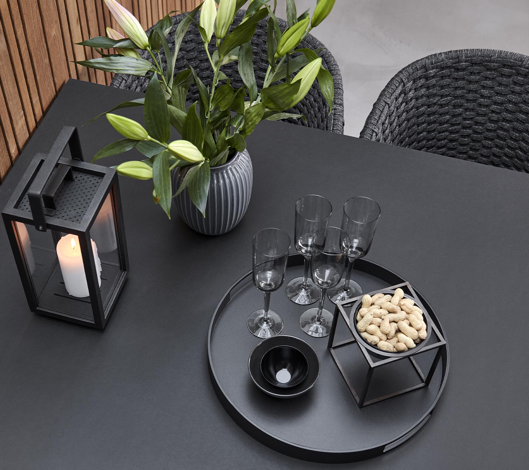 Une disposition de table élégante avec une lanterne, un vase avec des fleurs, des verres et un plateau de service avec des amuse-gueules.