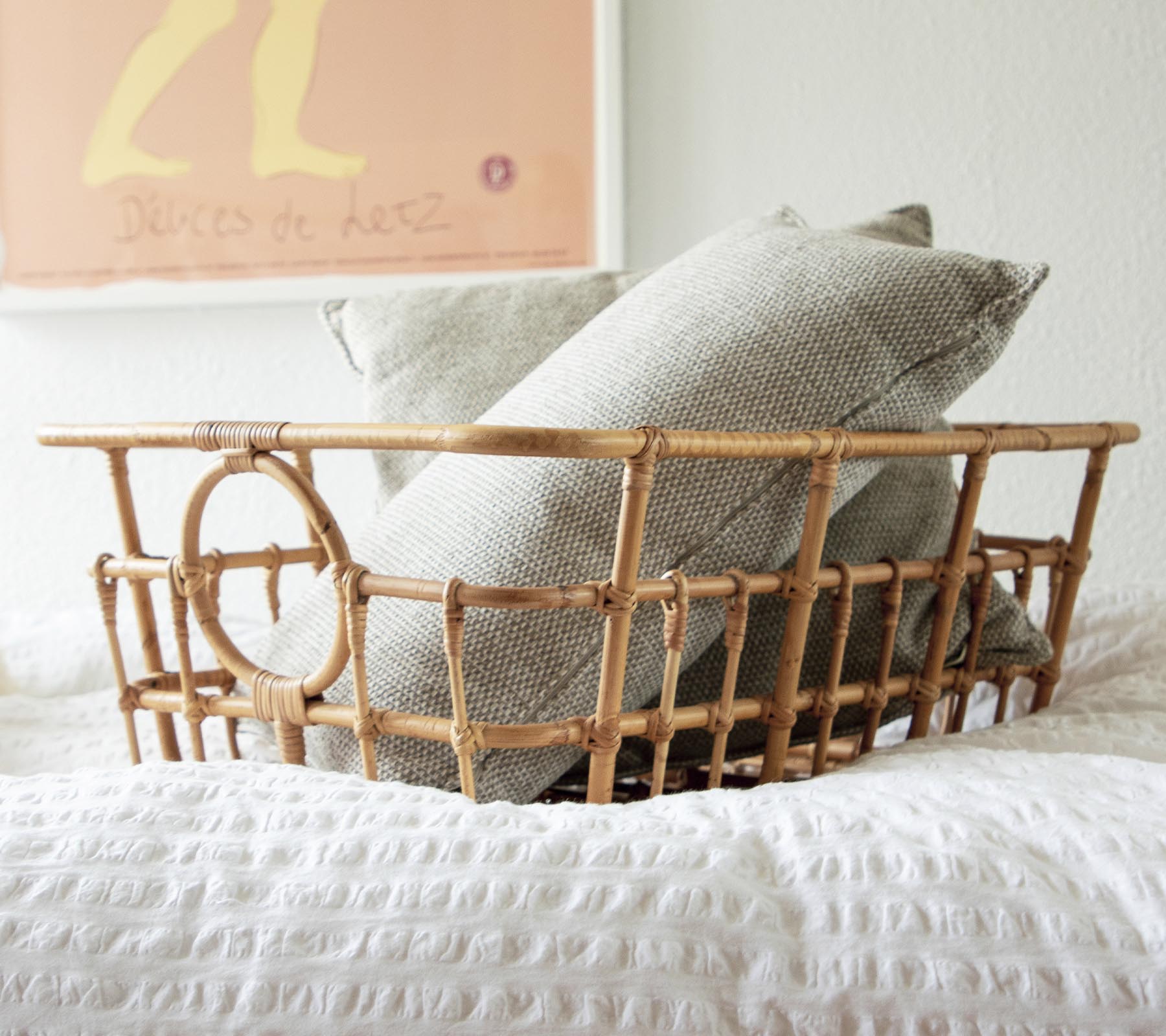 Panier en rotin avec des coussins gris et blancs dans un cadre de chambre à coucher cozy.