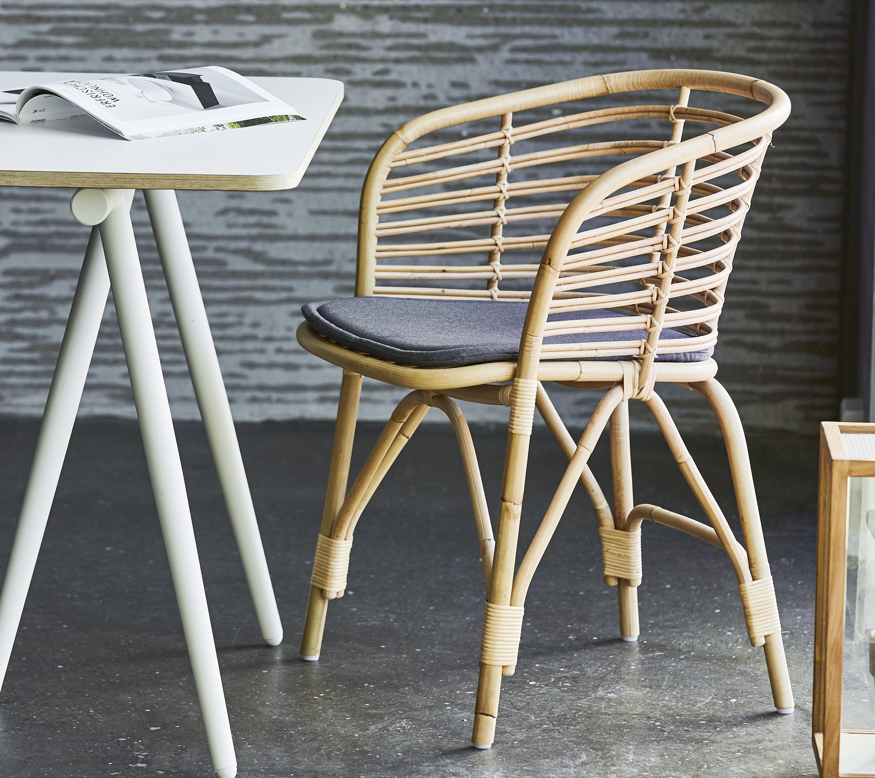 Chaise en osier élégante avec un coussin gris, associée à une table simple et une décoration contemporaine. Convient pour un seating décontracté et la détente.